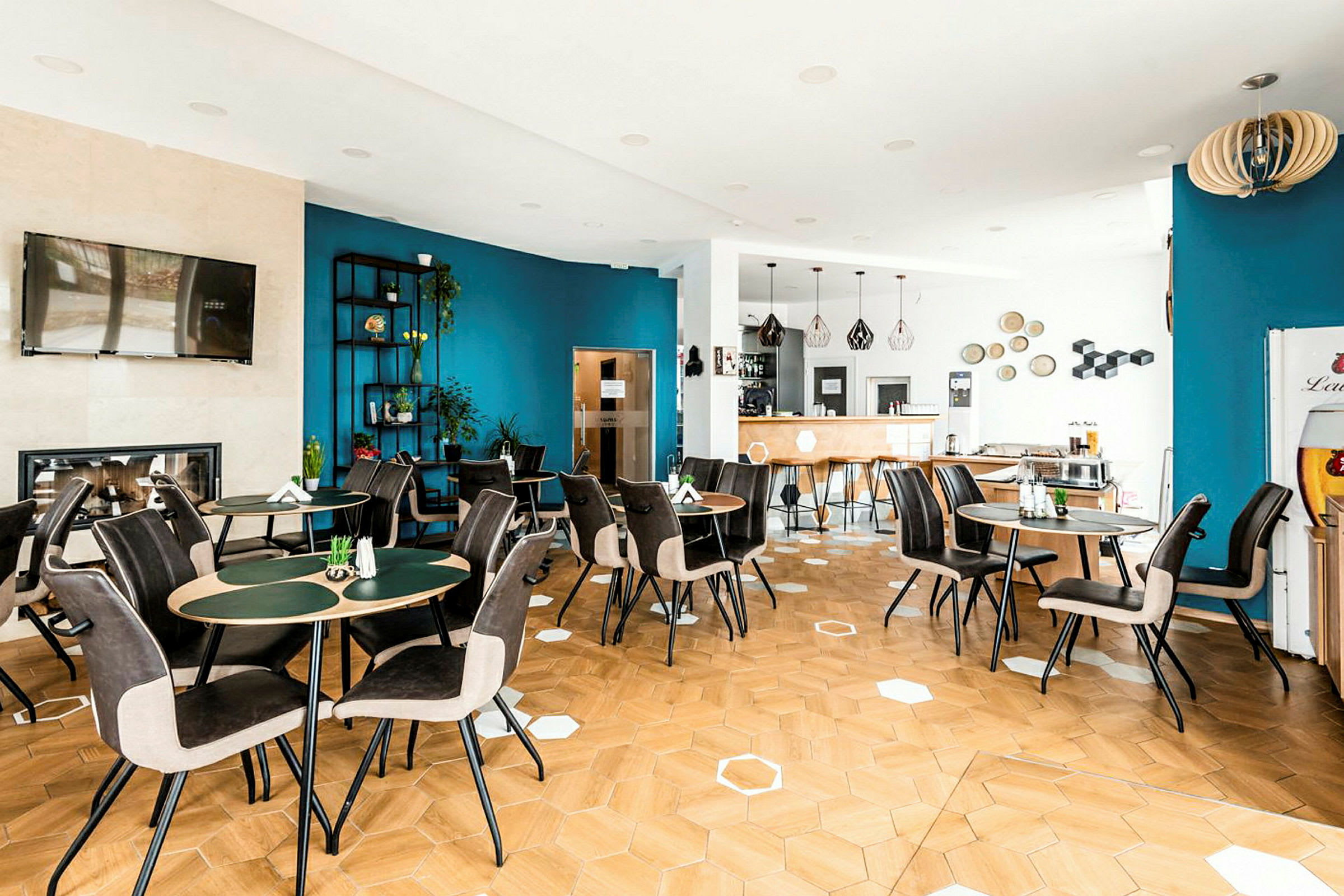 Bilde som viser en moderne innredet kafé med bord og stoler samt en blå vegg med dekorasjoner. (AI-generert tekst)
