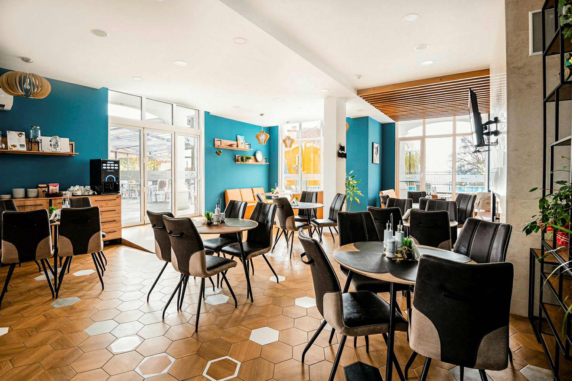 En lyst og moderne innredet kafé med blå vegger, hexagonformet tregulv og flere bord med komfortable stoler. (AI-generert tekst)