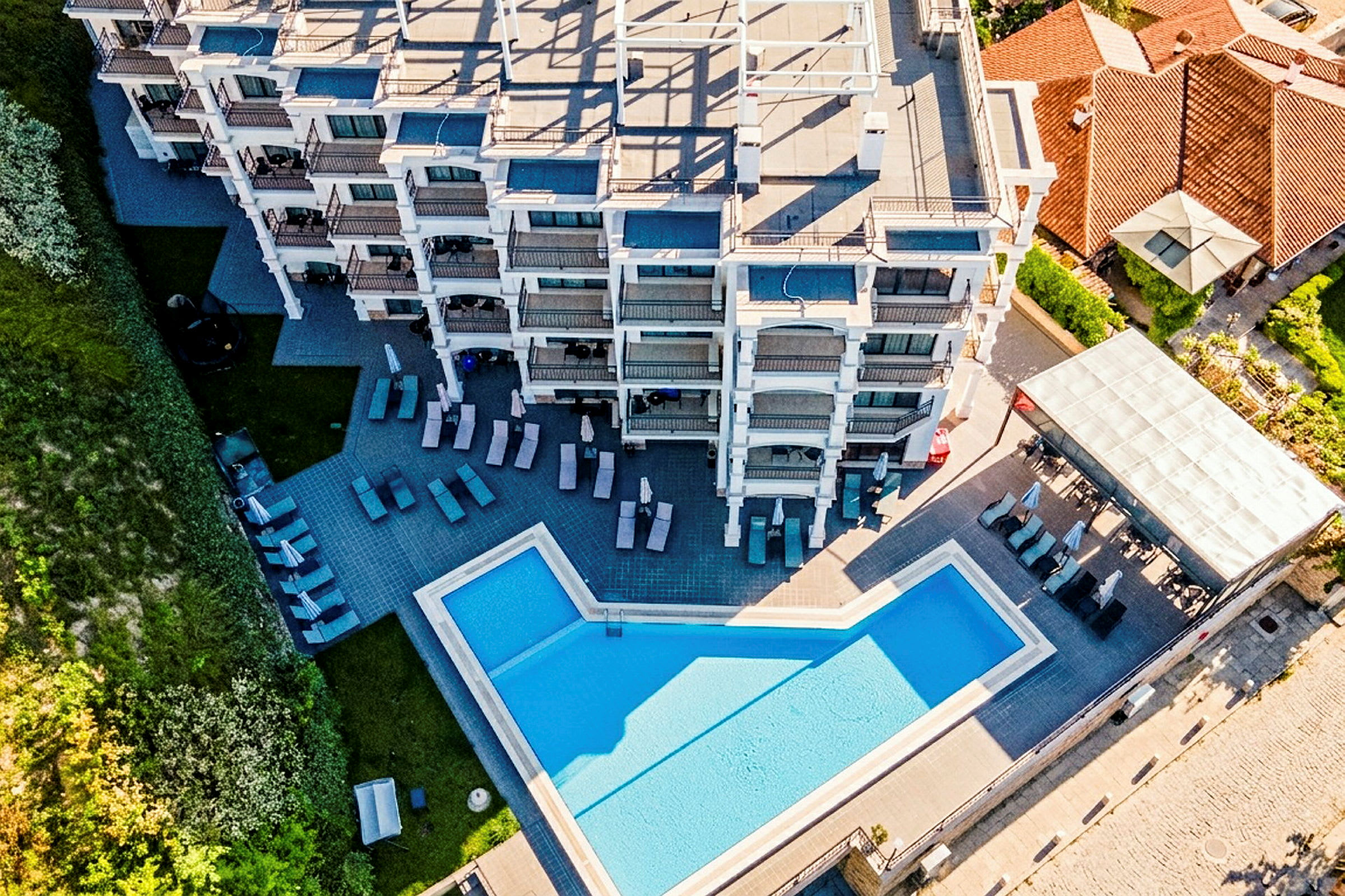 Flyfoto av en hotellbygning med et svømmebasseng og solsenger utendørs. (AI-generert tekst)