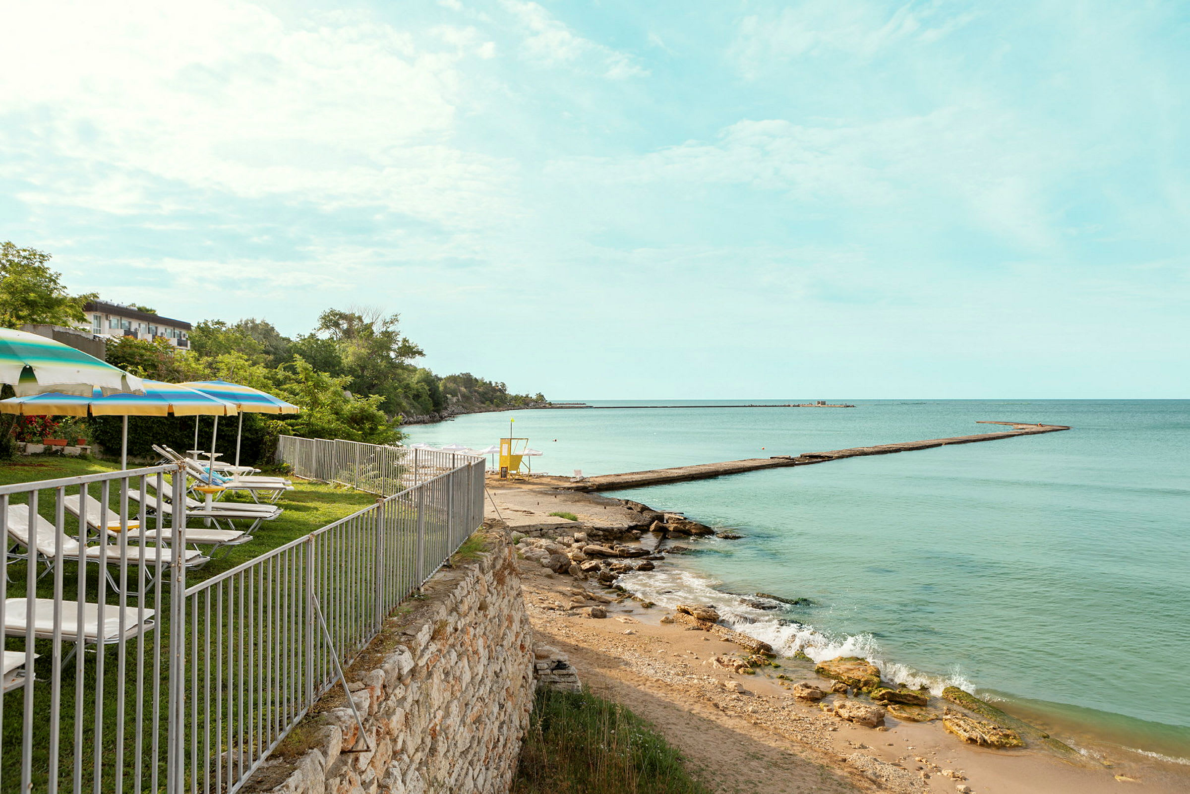 En strand med solsenger og parasoller ved et gjerde nær havet. (AI-generert tekst)