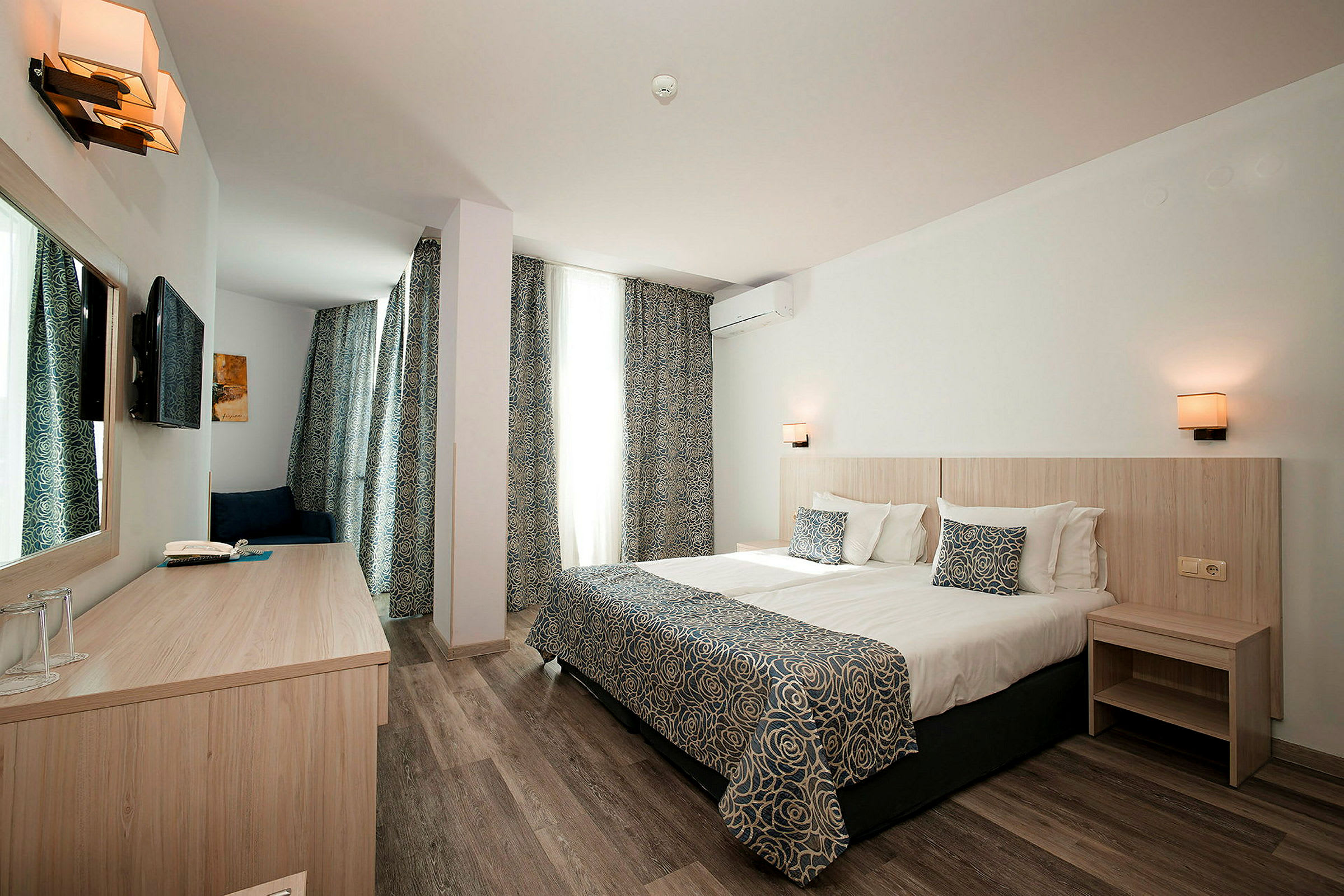 Hotellrom med en dobbeltseng, skrivebord og en TV på veggen. (AI-generert tekst)