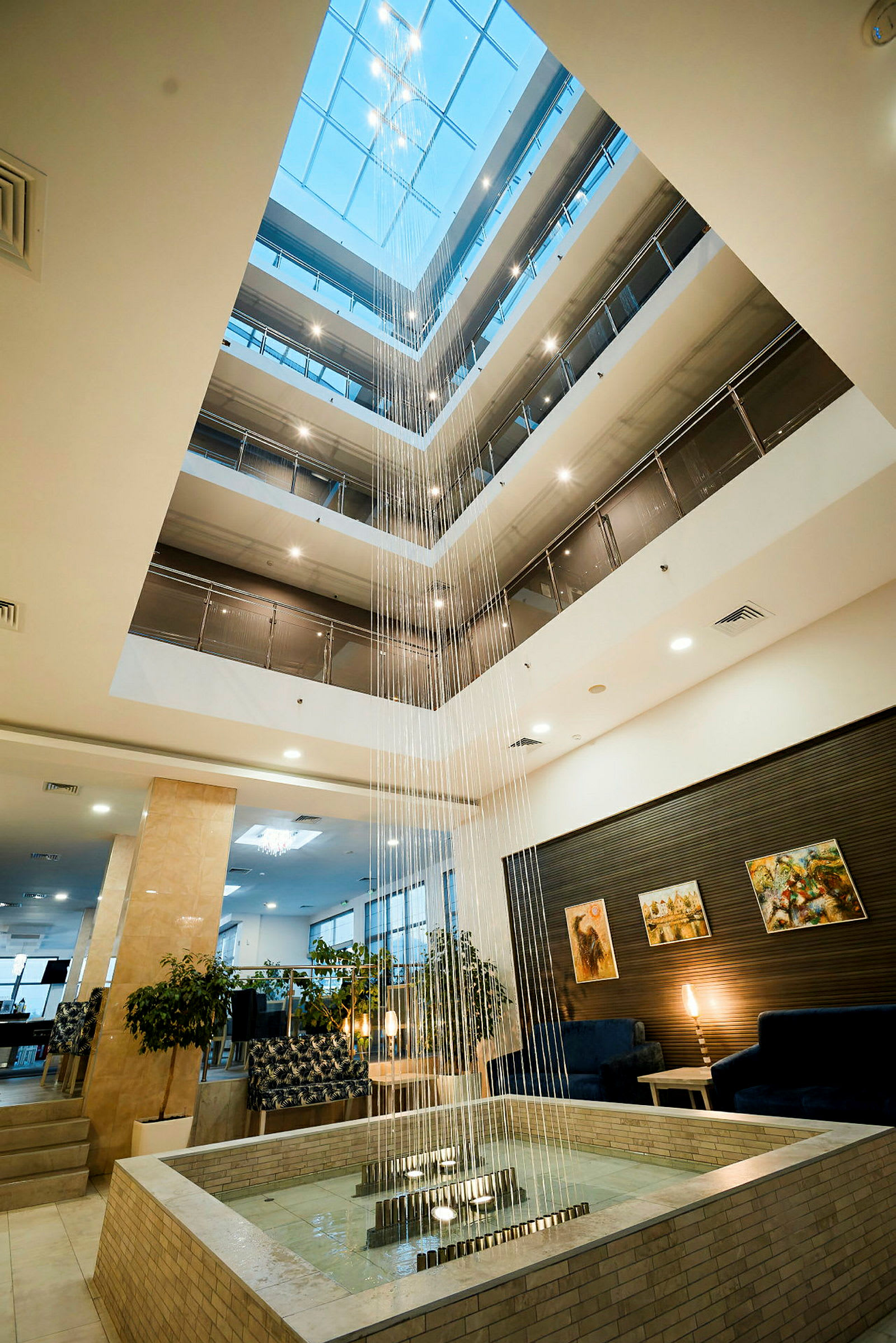 Et lyst og romslig hotellatrium med flere etasjer, dekorert med et fossefall i midten som renner inn i en fontene. (AI-generert tekst)