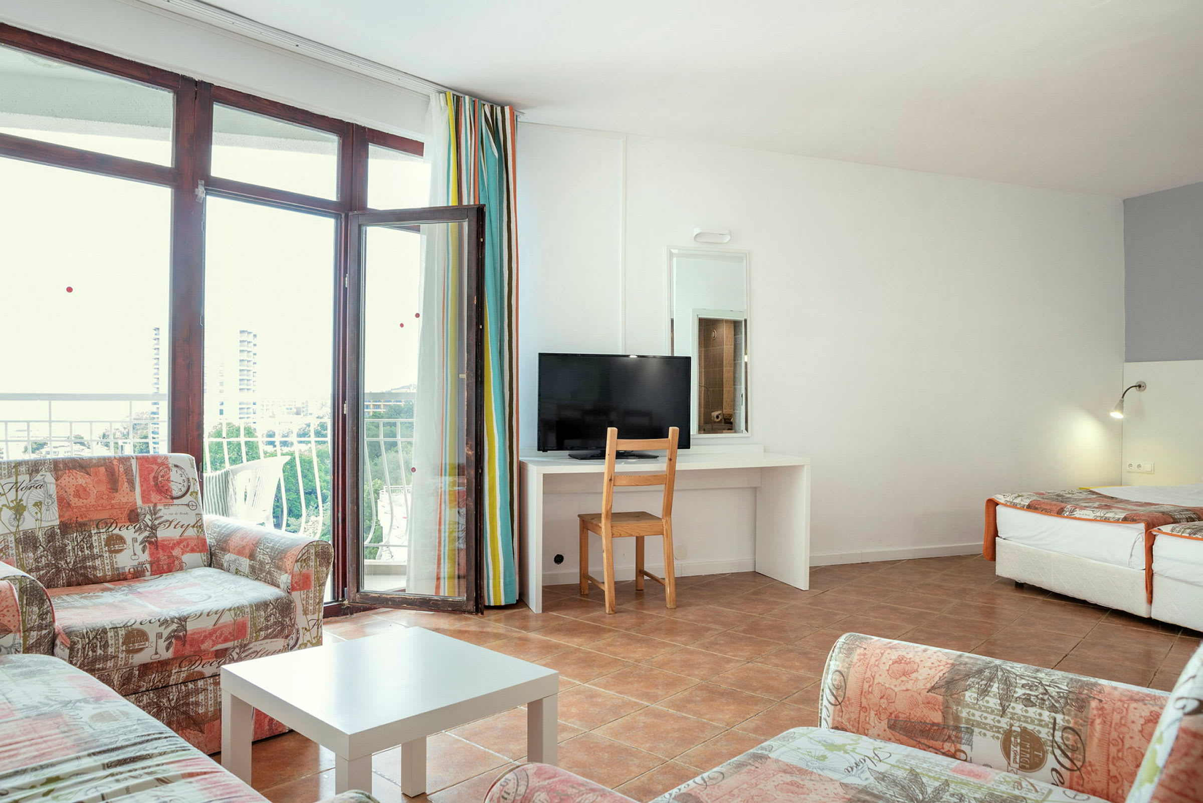 Et lyst hotellrom med sofa, bord og en balkong. (AI-generert tekst)