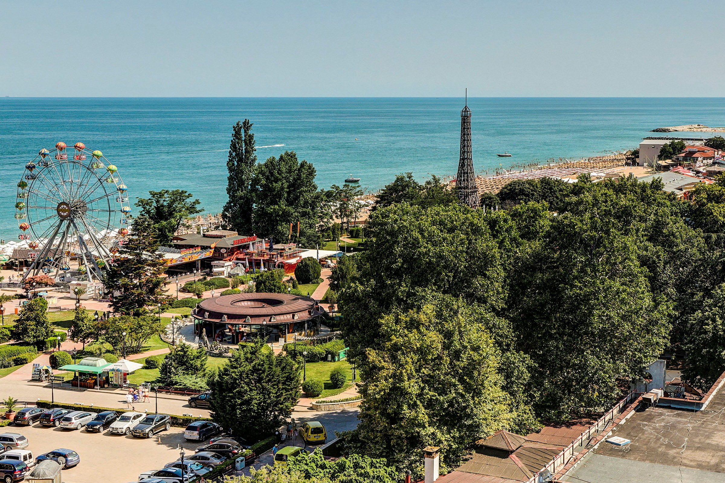 Utsikt over en fornøyelsespark og en strand ved havet, med et stort pariserhjul og grøntområder. (AI-generert tekst)