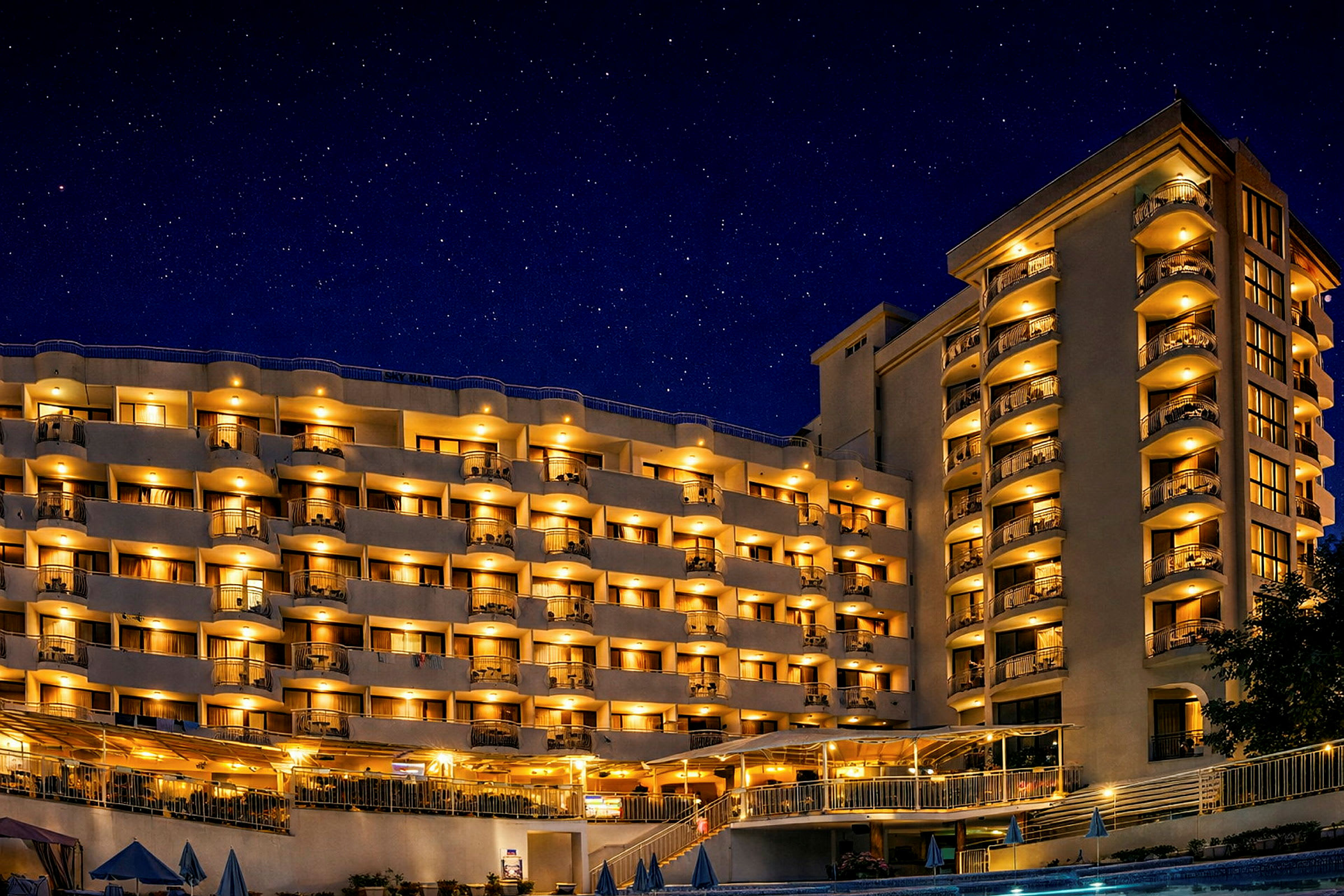 Hotellbygning med belyste balkonger og vinduer om kvelden under en stjerneklar nattehimmel. (AI-generert tekst)