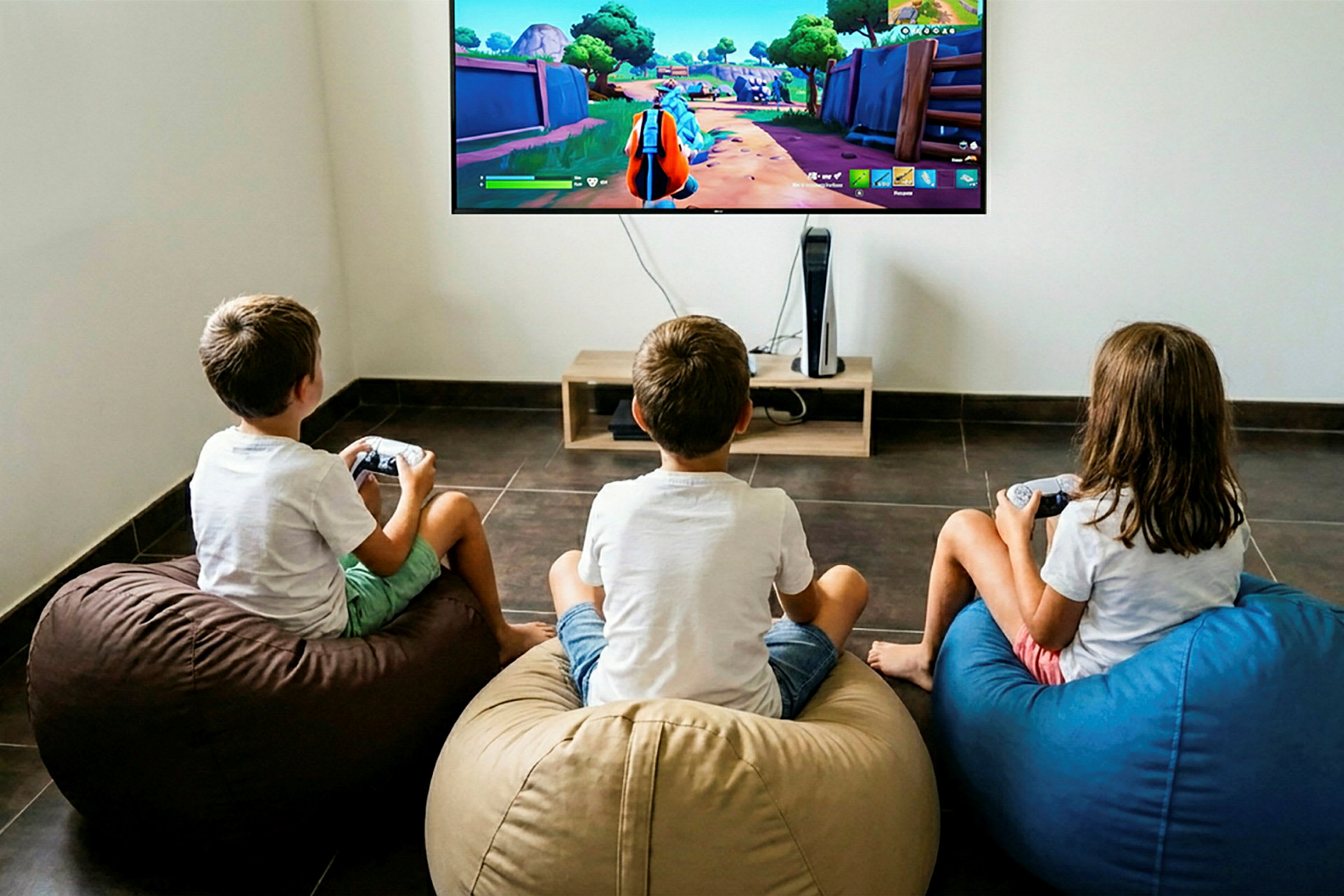 Tre barn sitter på sittesekker og spiller et videospill på en stor TV som er montert på veggen. (AI-generert tekst)