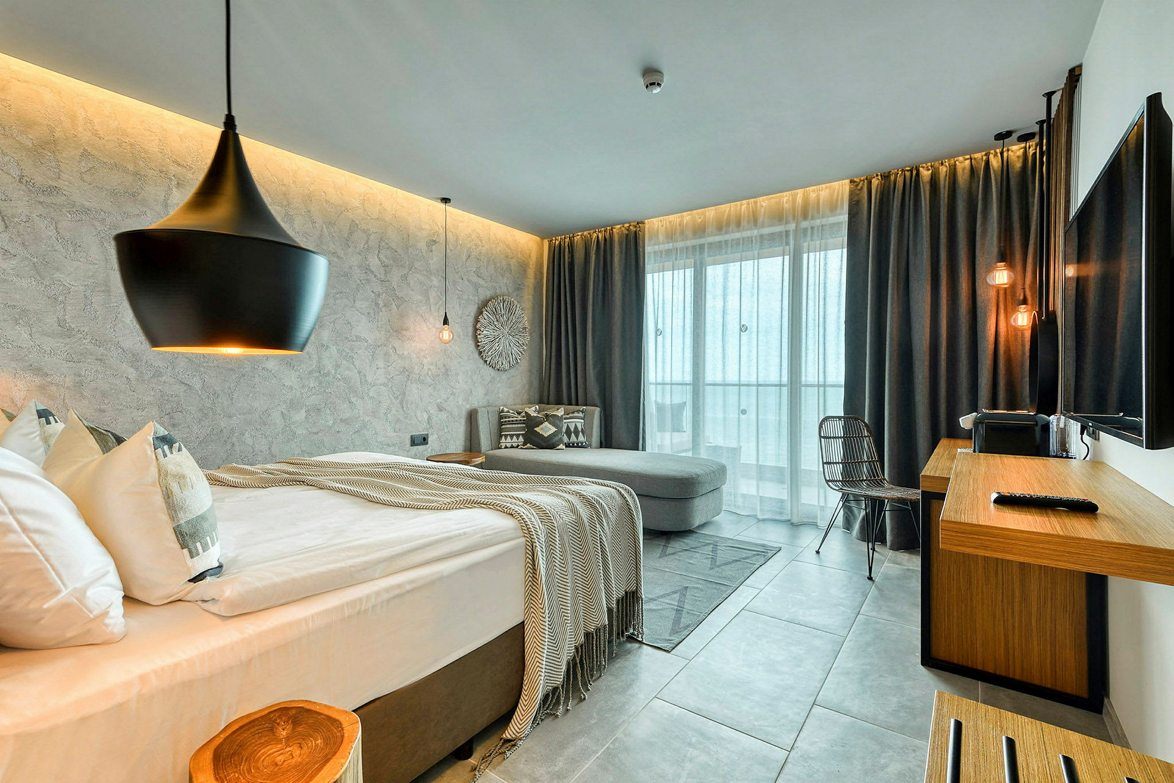Et moderne hotellrom med seng, sofa, skrivebord og store vinduer. (AI-generert tekst)