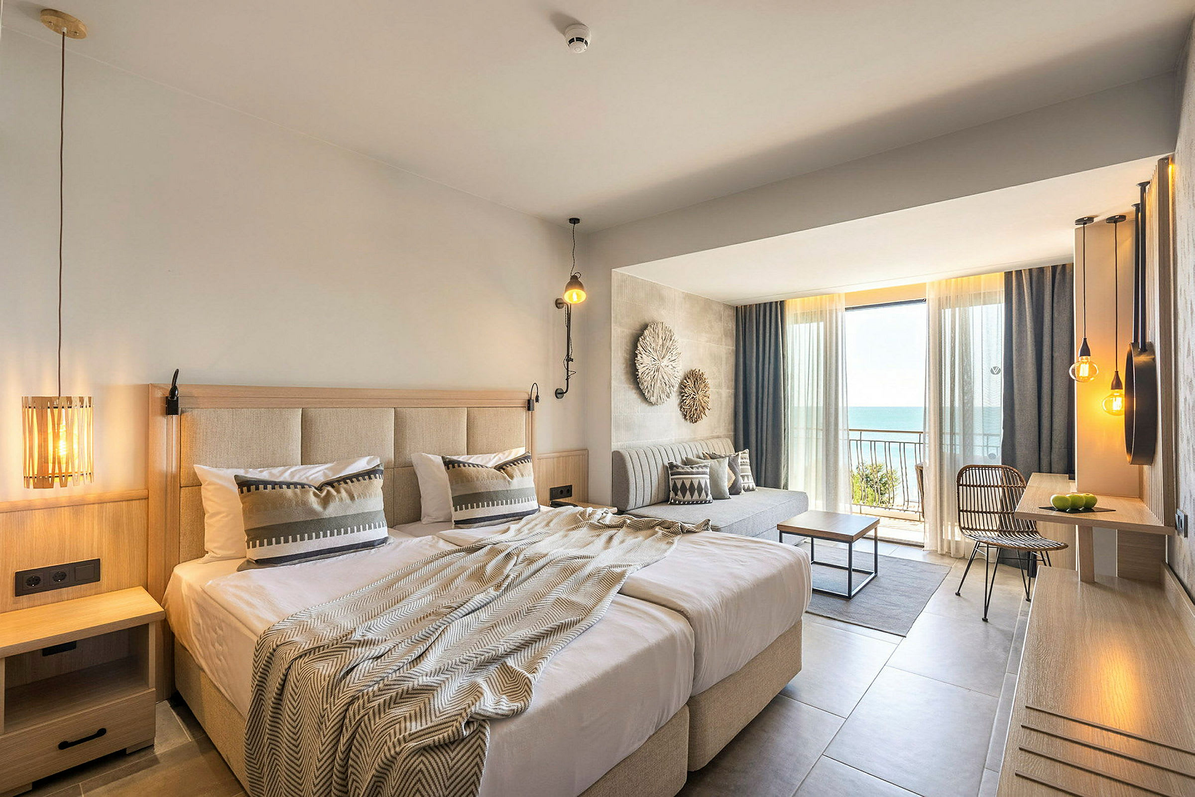 Hotellrom med dobbeltseng, sitteområde og balkong med utsikt over havet. (AI-generert tekst)