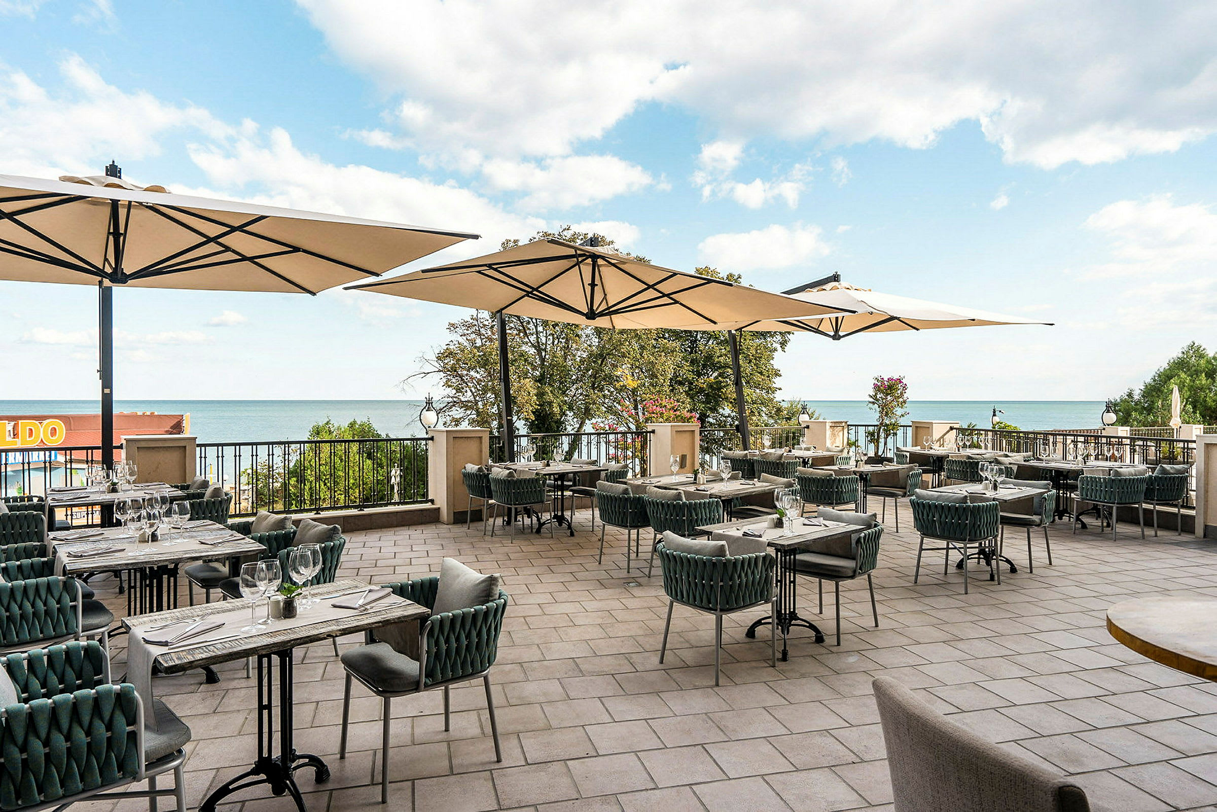 En terrasse med spisebord, stoler og parasoller, med utsikt mot havet. (AI-generert tekst)