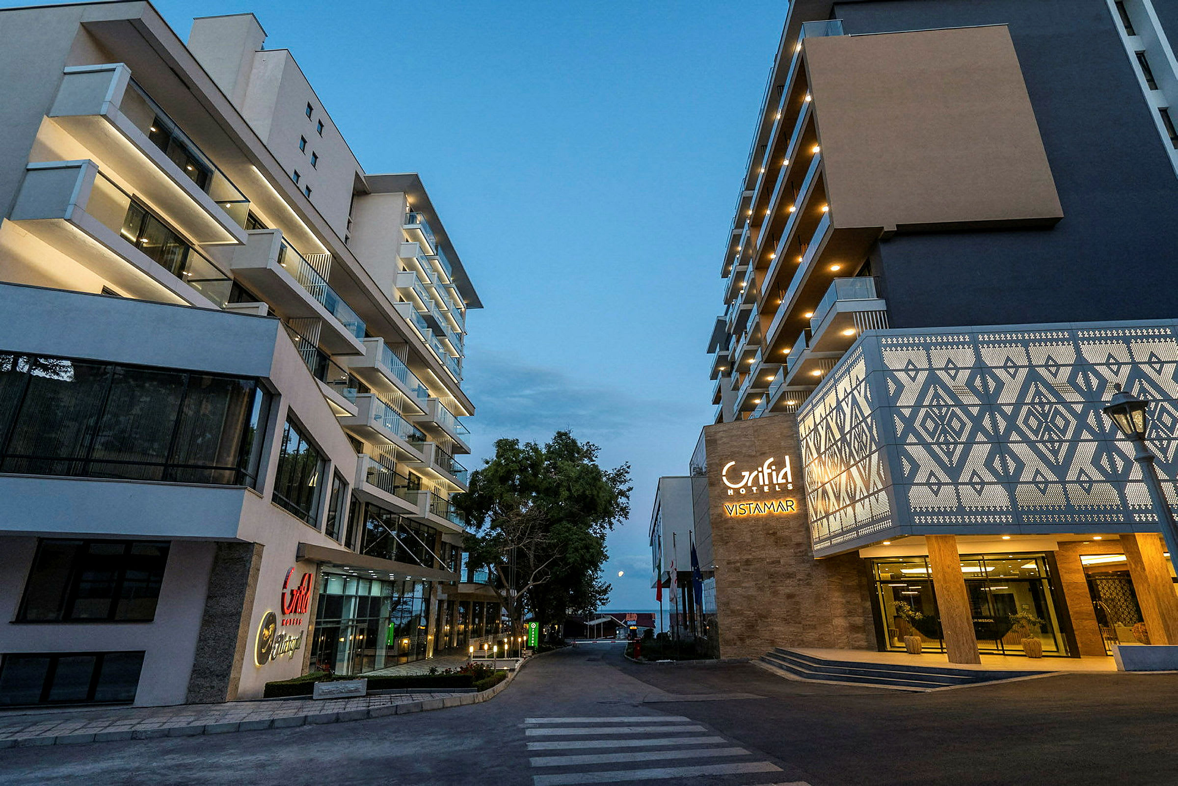 To moderne hotellbygninger ved en gangvei om kvelden. (AI-generert tekst)