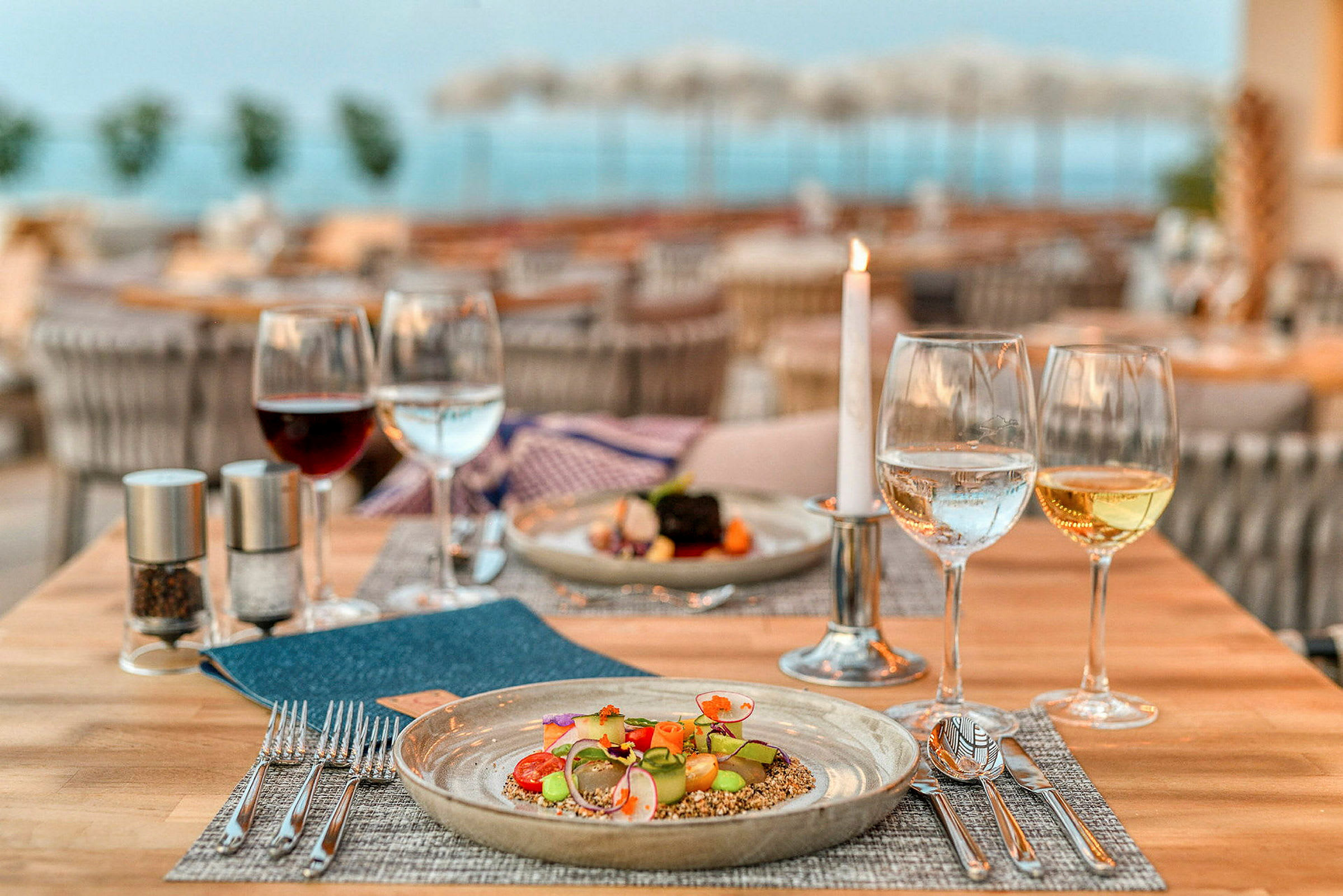 Et dekket restaurantbord med en tallerken mat og glass med vin, vann og et tent lys. (AI-generert tekst)