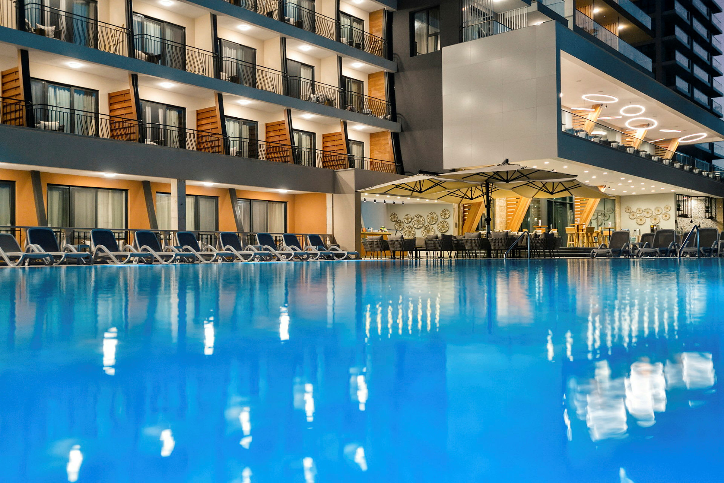 Et hotell med et utendørsbasseng, omkringliggende solsenger og en restaurant med tak og bordservering. (AI-generert tekst)