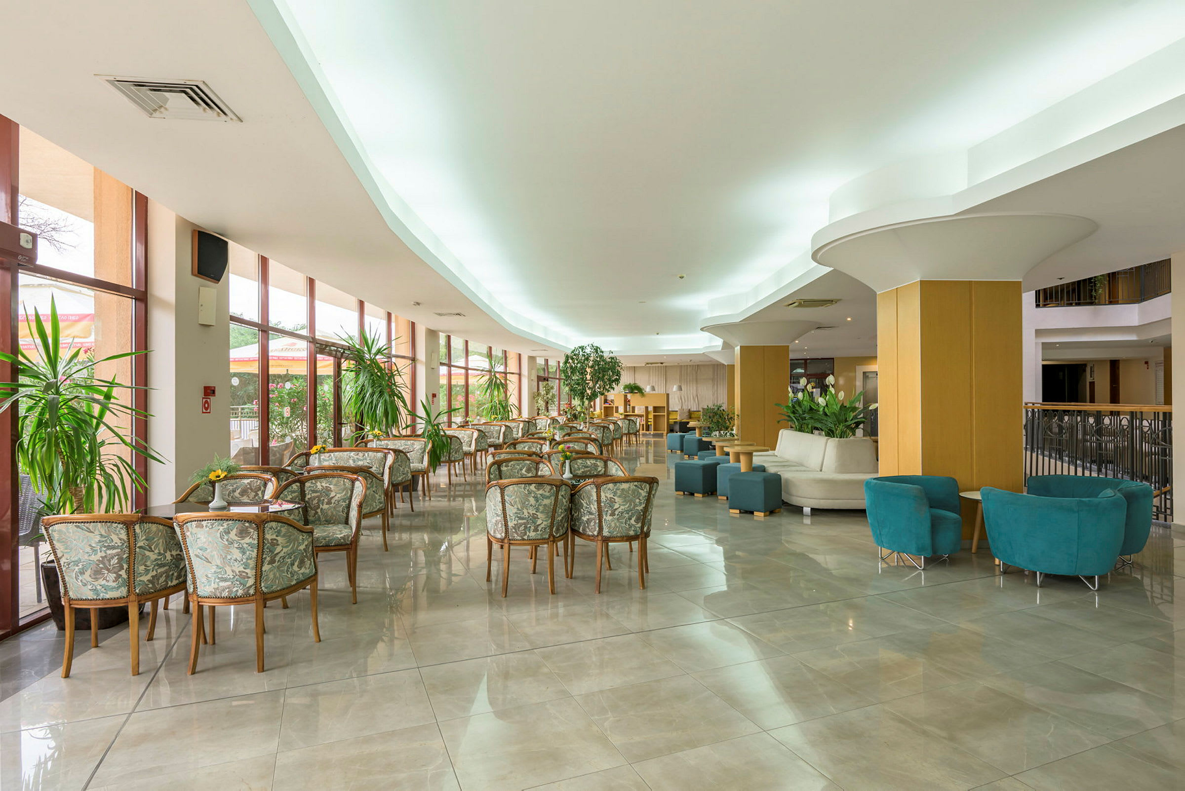 Hotellobby med bord og stoler samt grønne planter. (AI-generert tekst)