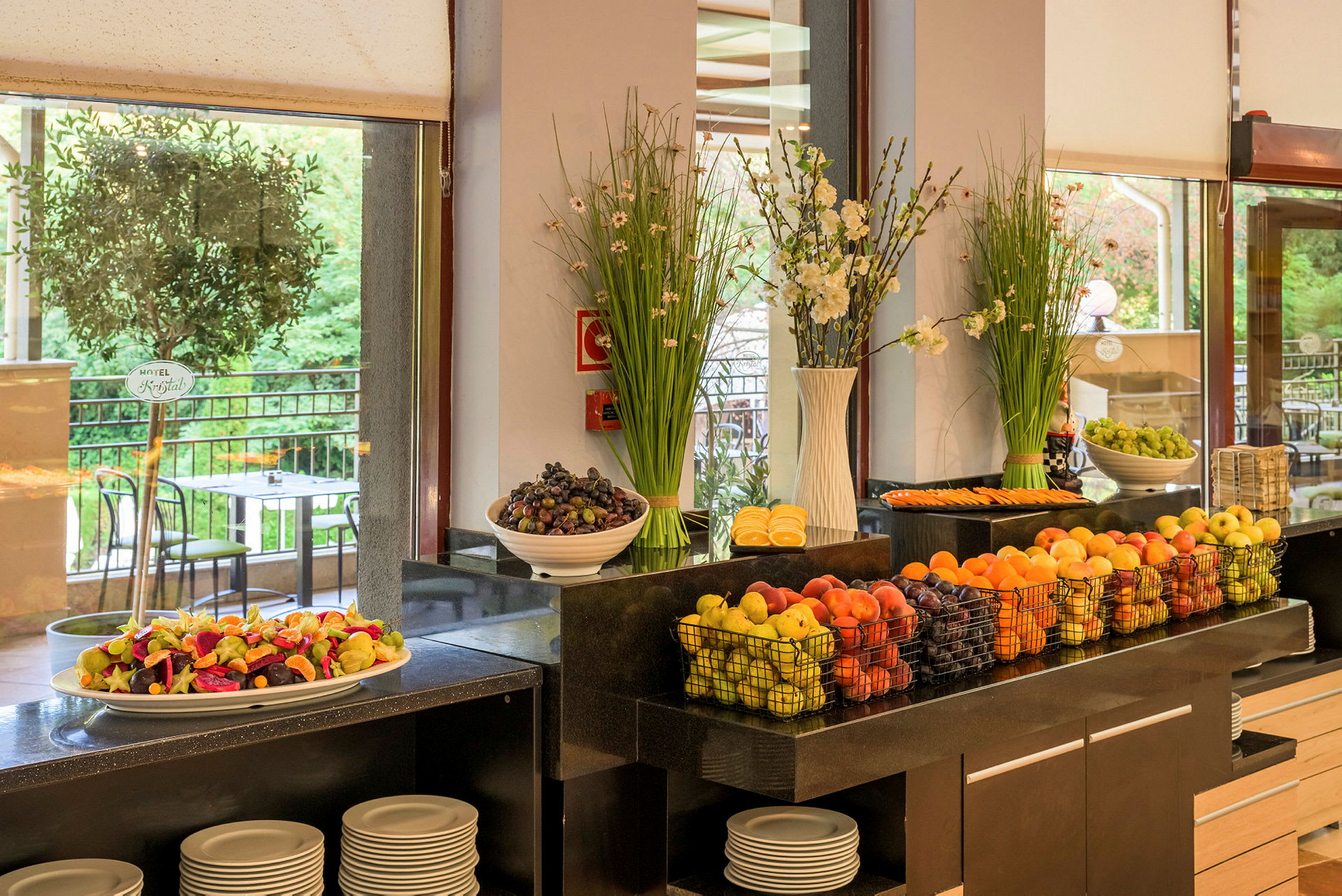 Bilde av en buffé med fersk frukt og dekorasjoner, samt utsikt mot en terrasse. (AI-generert tekst)