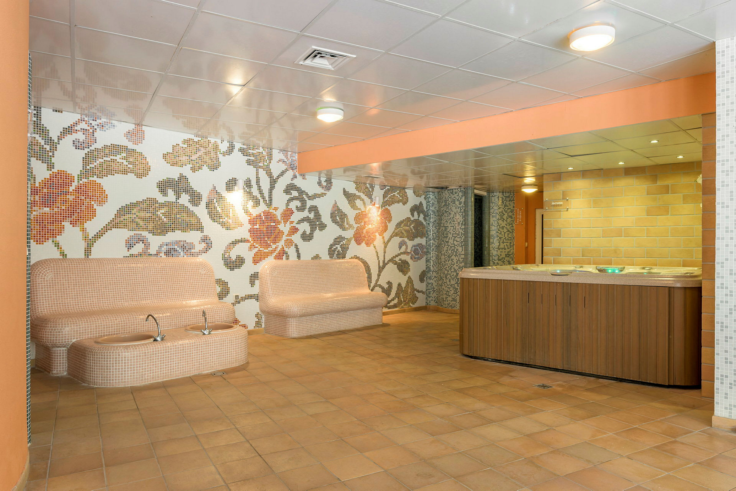 Interiør av et spaområde med sitteplasser, detaljert mønster på veggene og en jacuzzi. (AI-generert tekst)