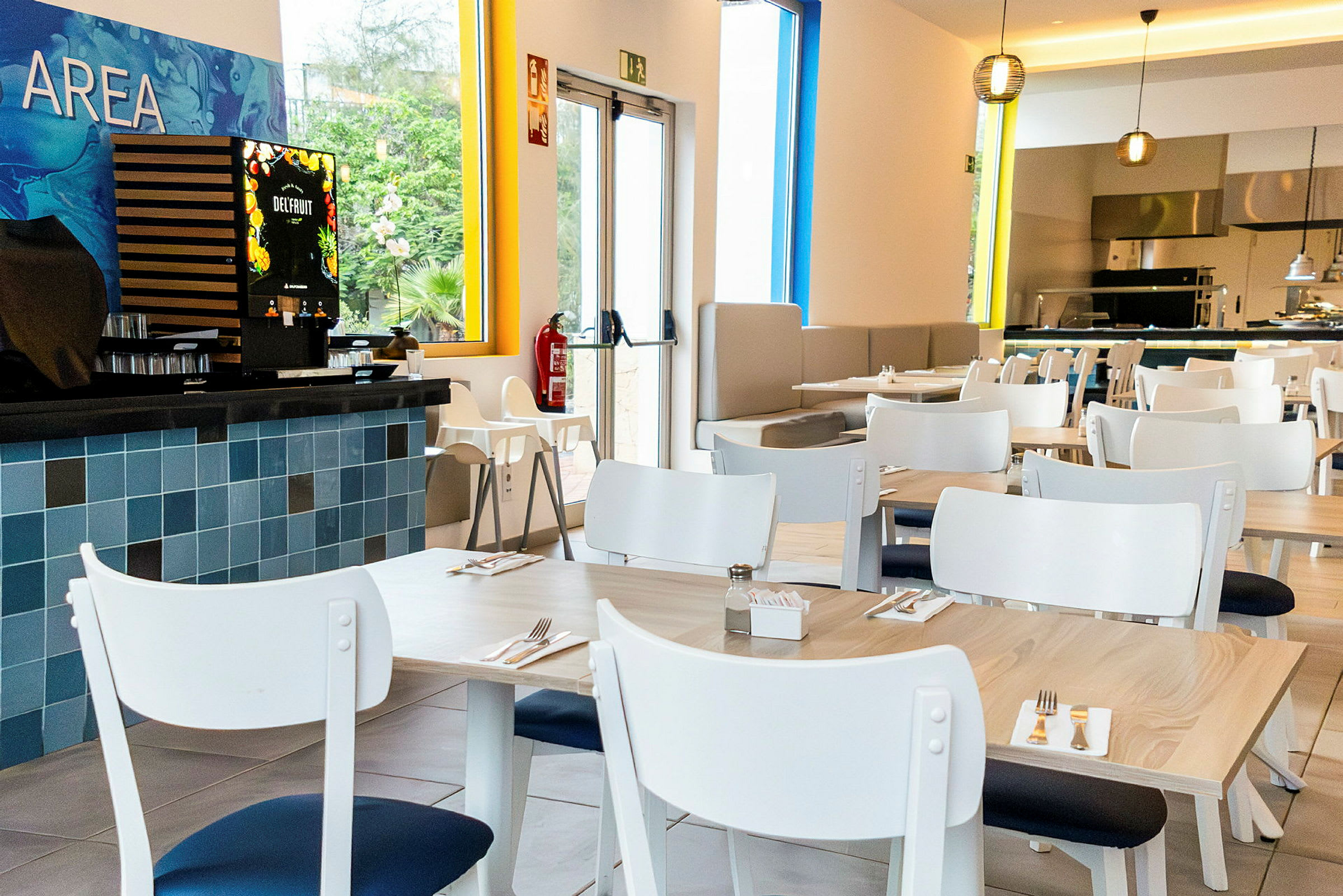 En moderne restaurant med hvite bord og stoler. En juiceautomat er synlig til venstre. (AI-generert tekst)