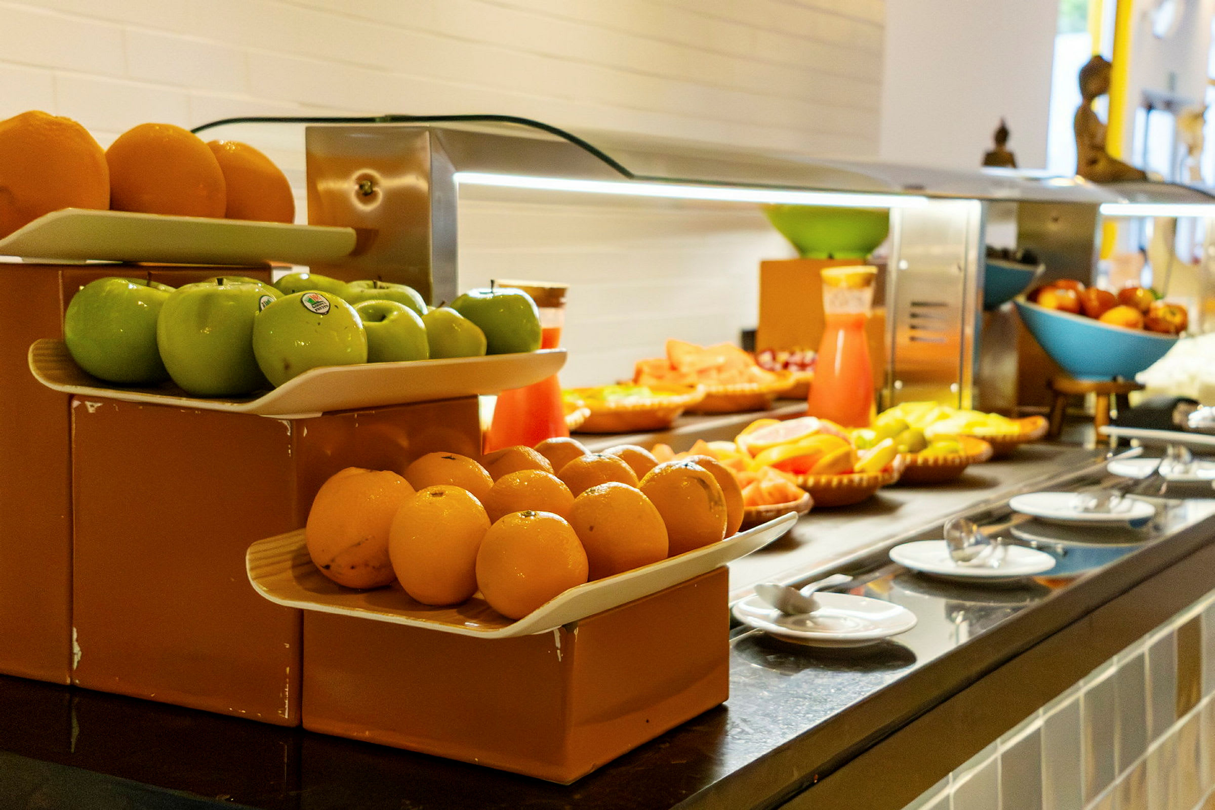 Fruktbuffet med grønne epler, appelsiner og annen frukt samt en juicekanne. (AI-generert tekst)