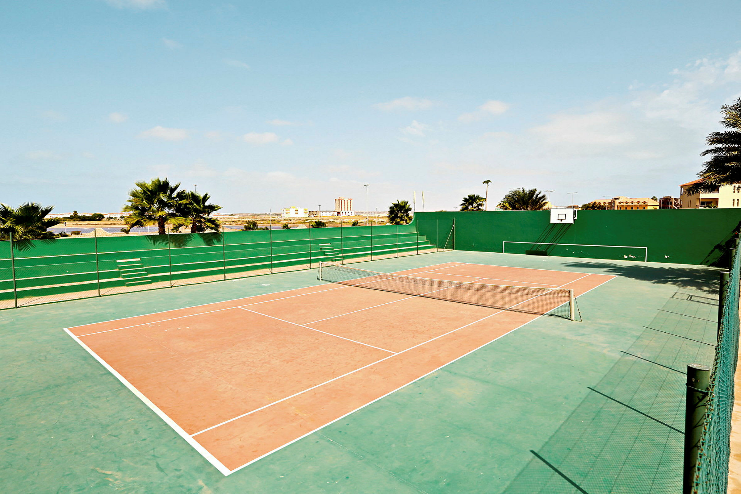 Utendørs tennisbane med grønn omgivende vegg og basketballkurv. (AI-generert tekst)