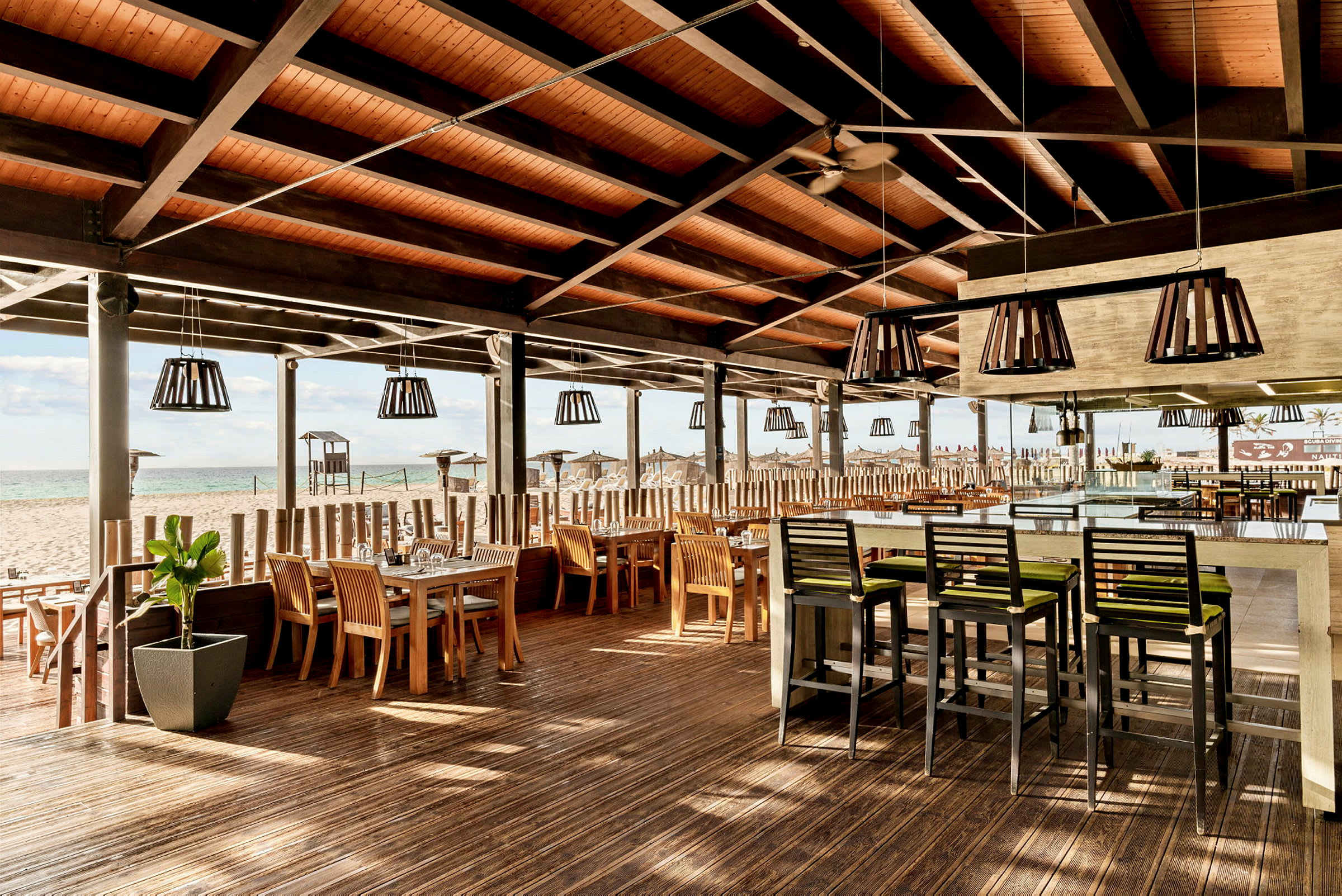 Utendørs restaurant med tak, trémøbler og bord ved en strand. (AI-generert tekst)