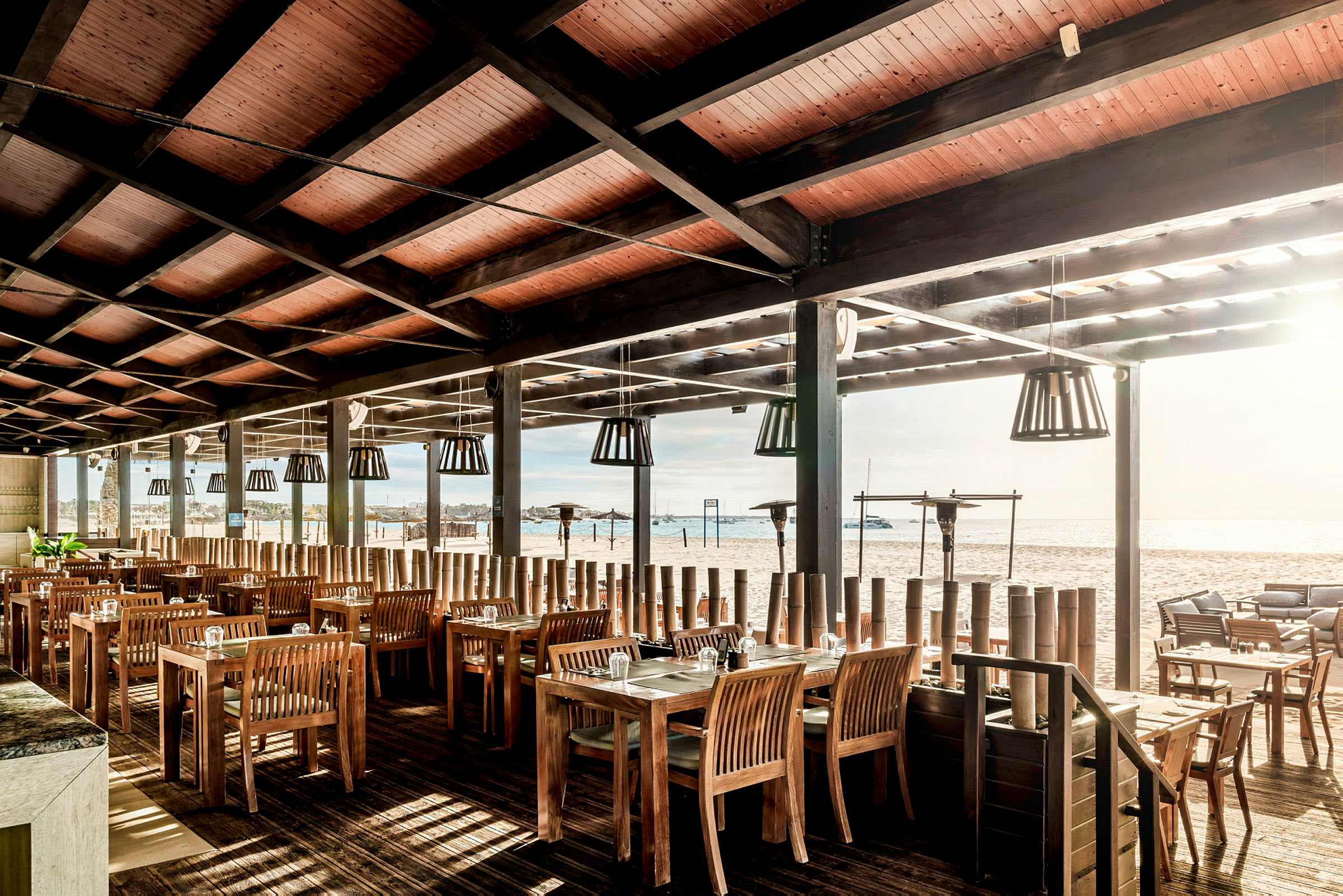 Restaurant med tremøbler og tak, ved stranden med utsikt over vannet. (AI-generert tekst)