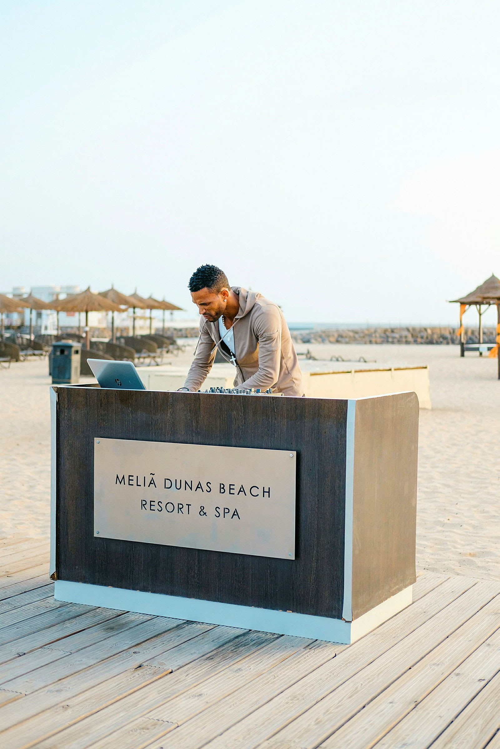 En person står ved et bord med teksten 'Meliã Dunas Beach Resort & Spa' ved stranden. (AI-generert tekst)