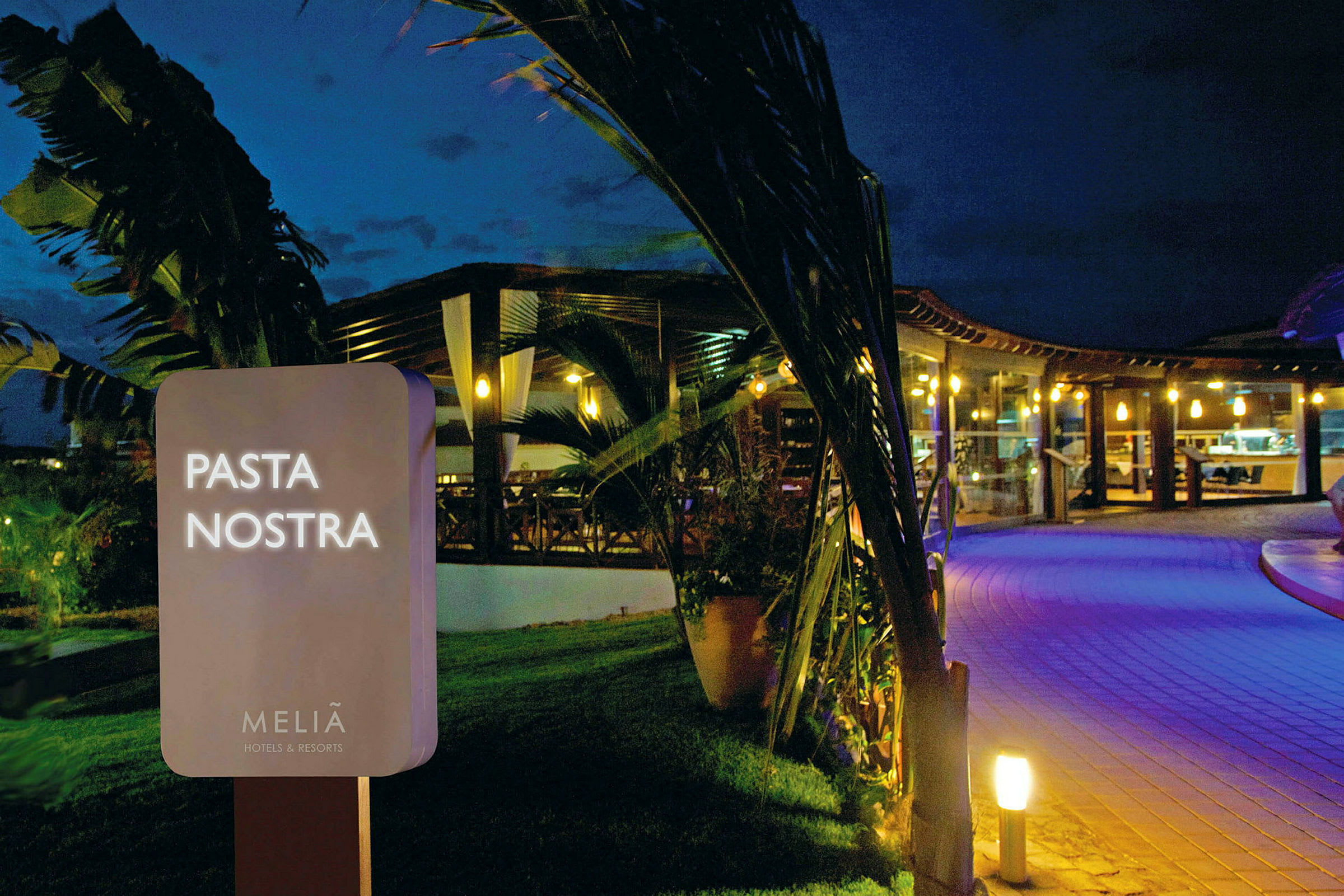 Skilt med teksten 'Pasta Nostra' foran en opplyst restaurant om kvelden. (AI-generert tekst)