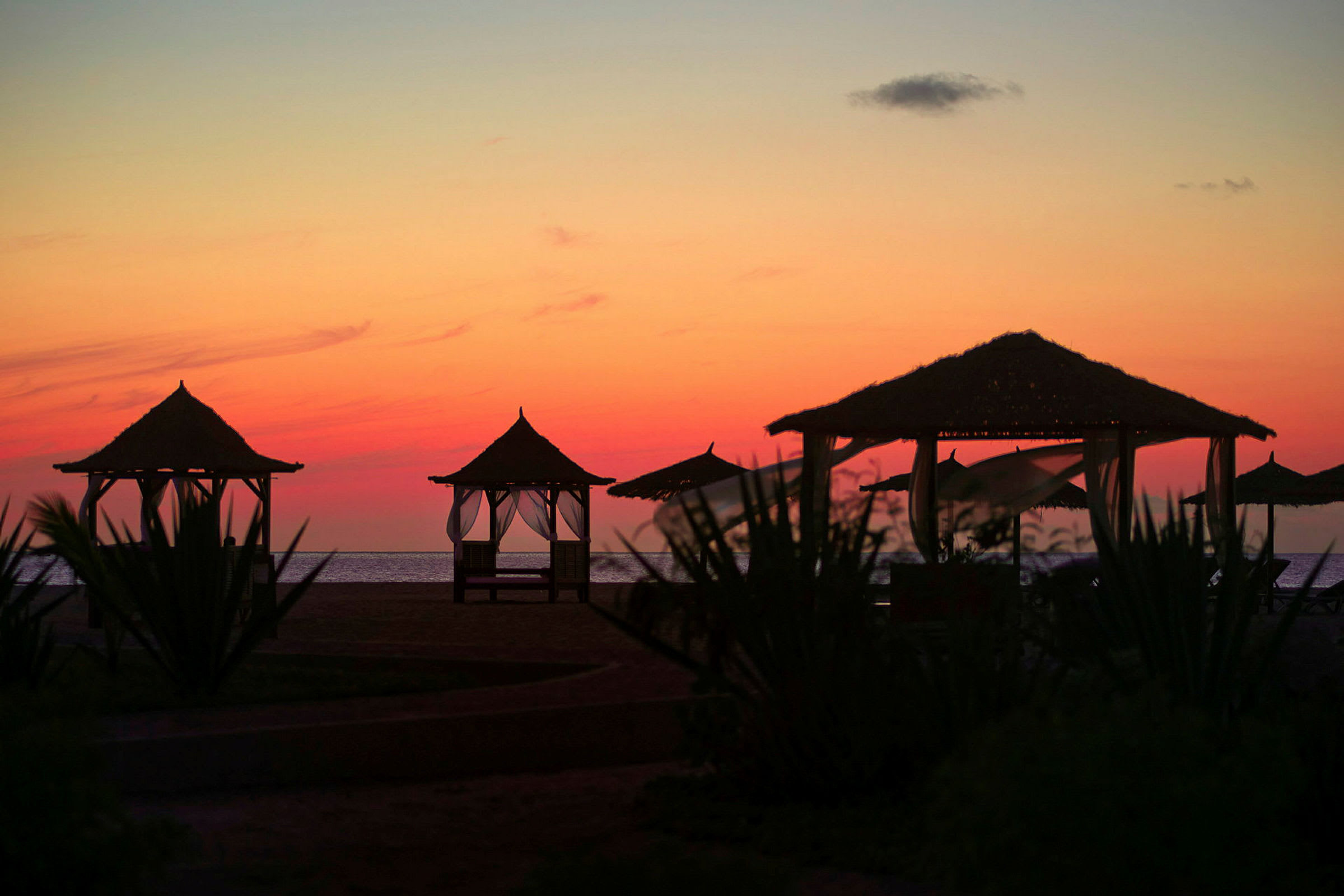 Bilde av en strand med solnedgang, hvor flere strandhytter er synlige i forgrunnen. (AI-generert tekst)