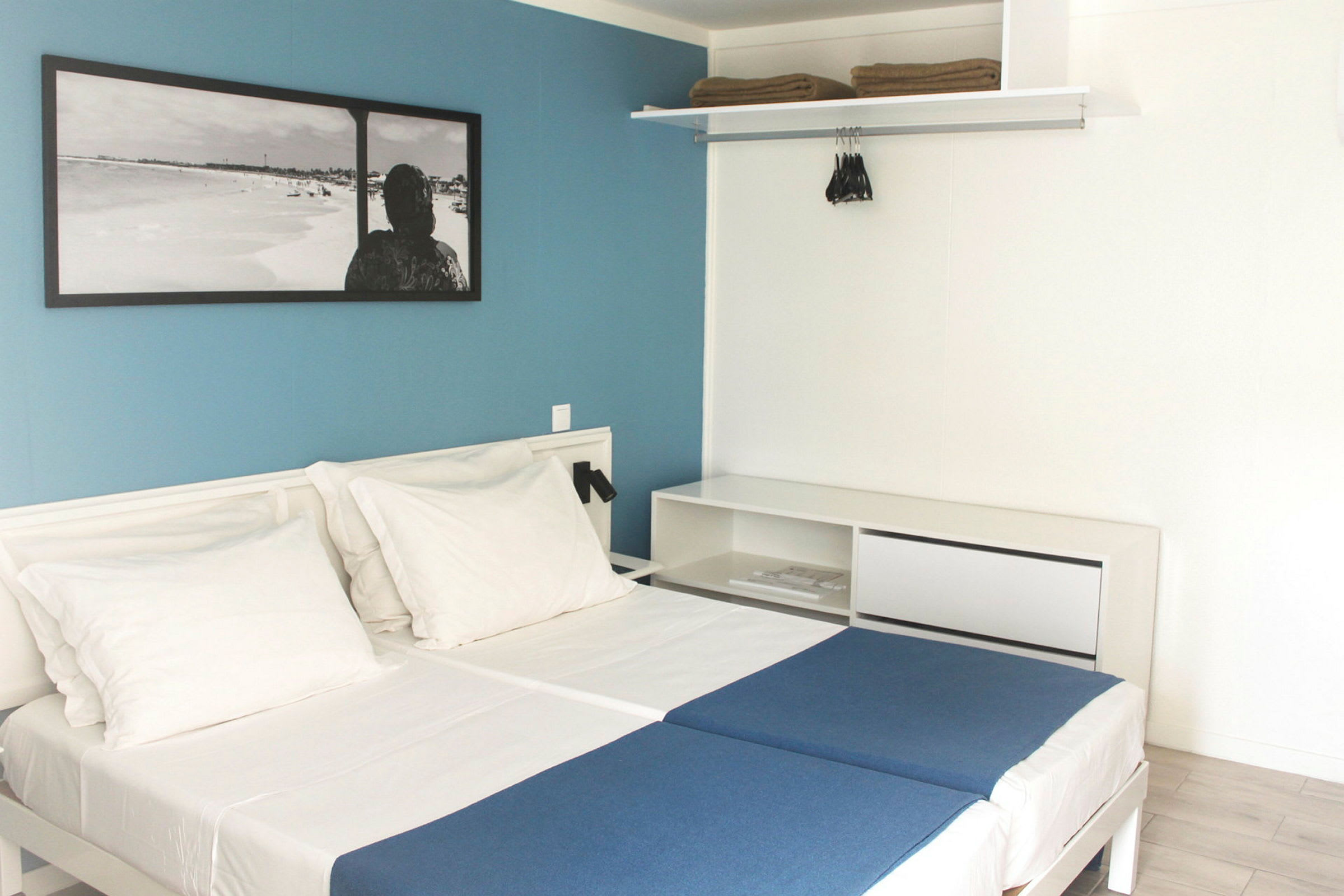 Hotellrom med to enkeltsenger, hvite vegger og en blå kontrastvegg. (AI-generert tekst)