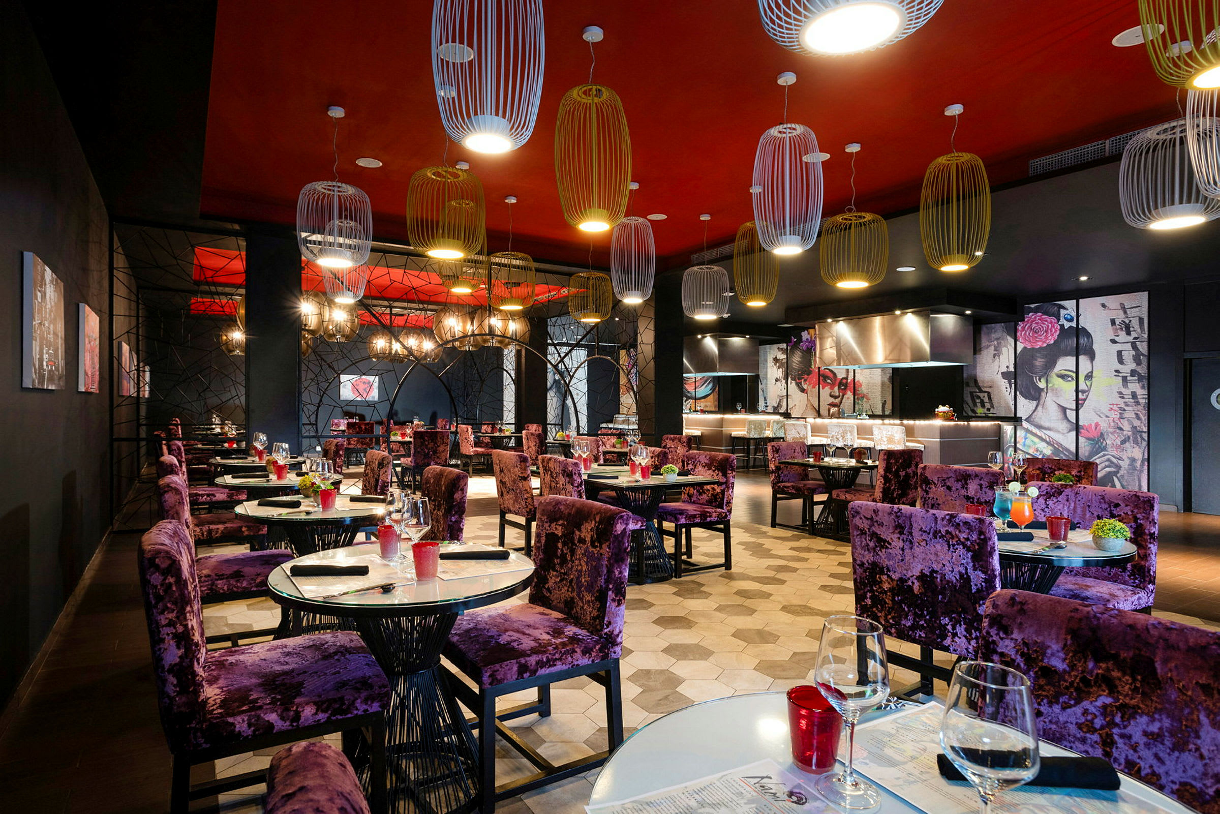 En restaurant med elegant innredning og lilla stoler ved dekkede bord. Veggene har kunstneriske motiver og taket er dekorert med moderne lamper. (AI-generert tekst)