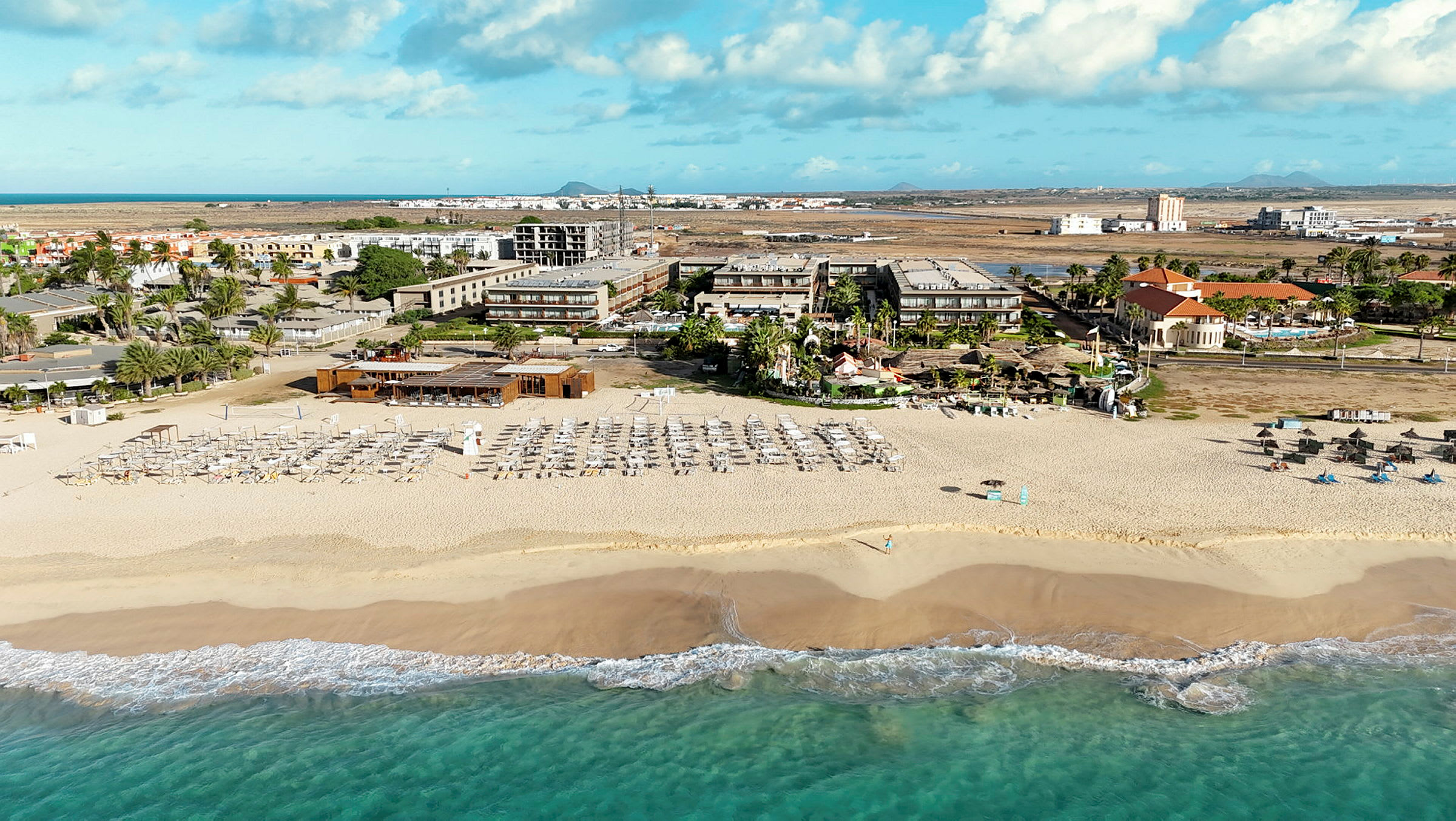 Bilde av en sandstrand med solsenger og parasoller, hotellbygninger i bakgrunnen. (AI-generert tekst)