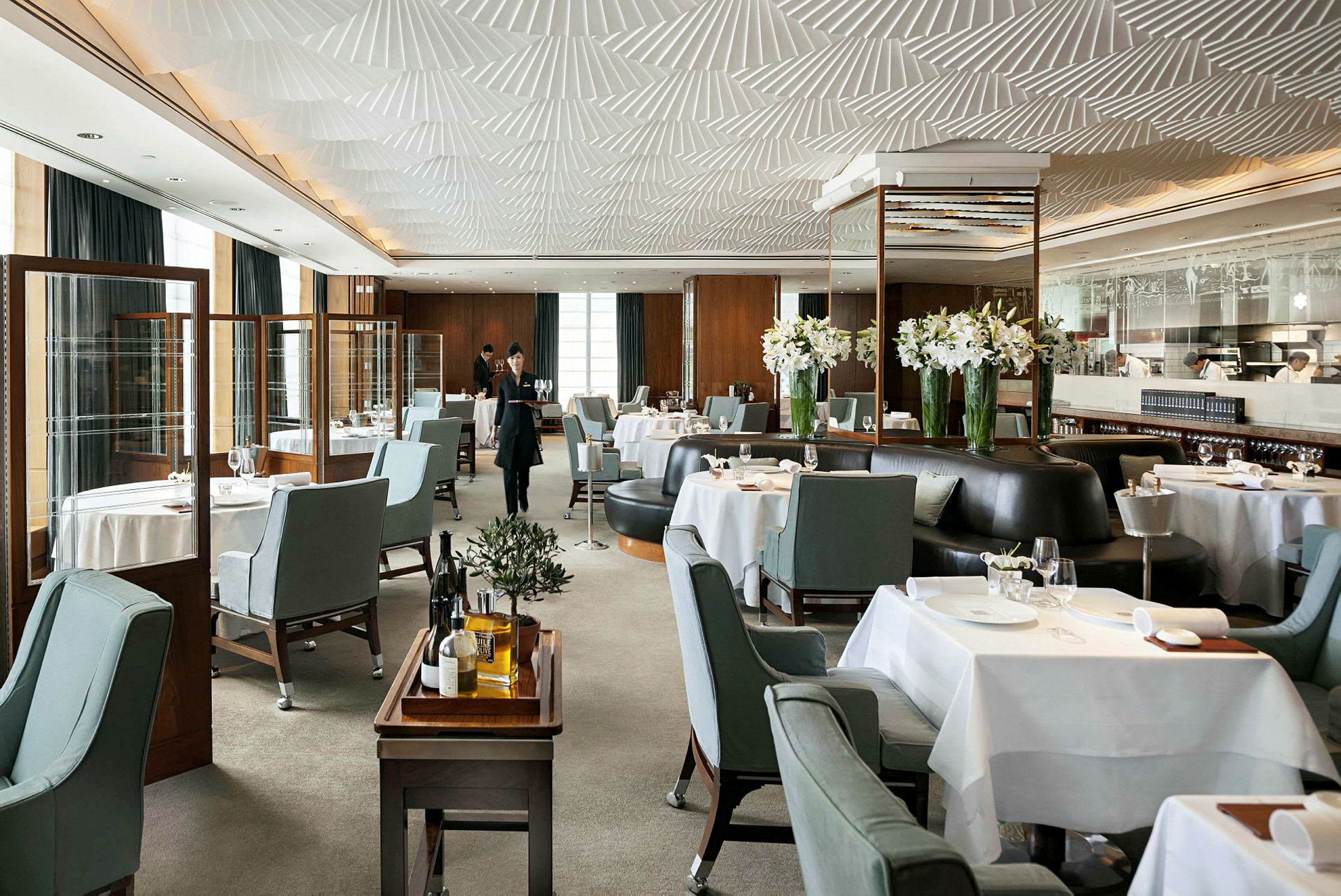 Det er en elegant restaurant med ferdigdekkede bord, blågrå stoler og dekorasjoner med hvite blomster. (AI-generert tekst)