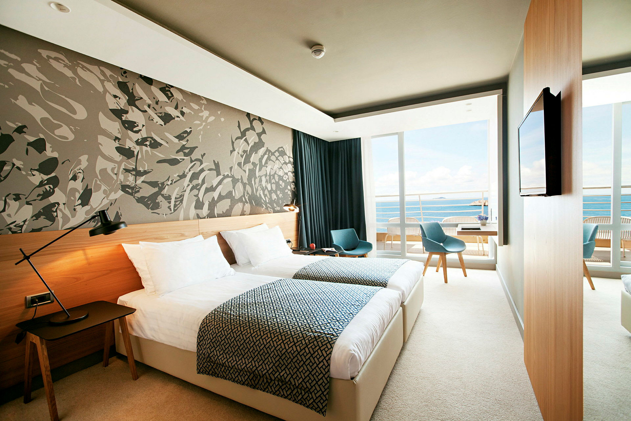 Et moderne hotellrom med to enkeltsenger, en veggdekorasjon og en balkong med utsikt over havet. (AI-generert tekst)