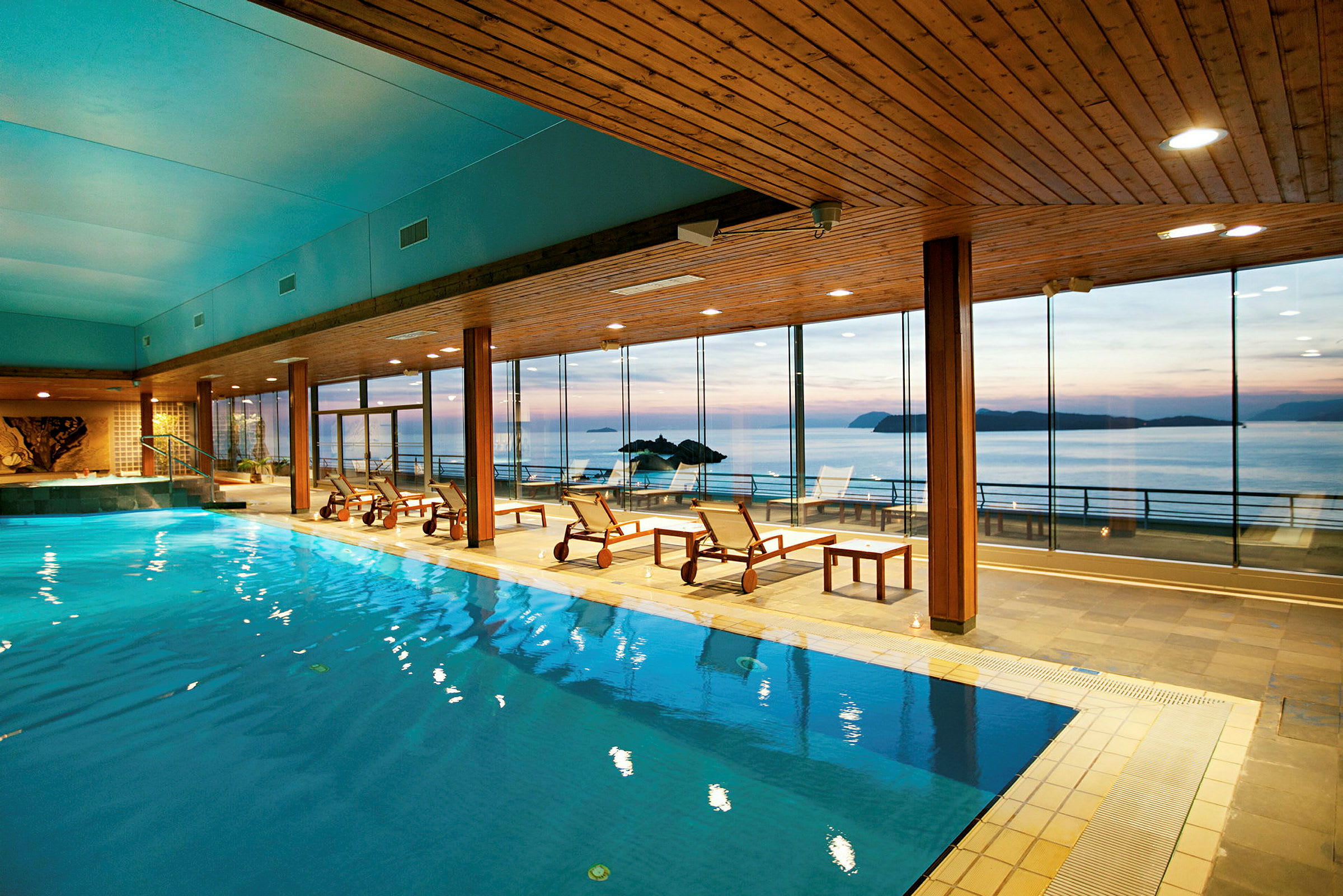 Et innendørsbasseng på et spa med utsikt over havet gjennom store panoramavinduer. (AI-generert tekst)