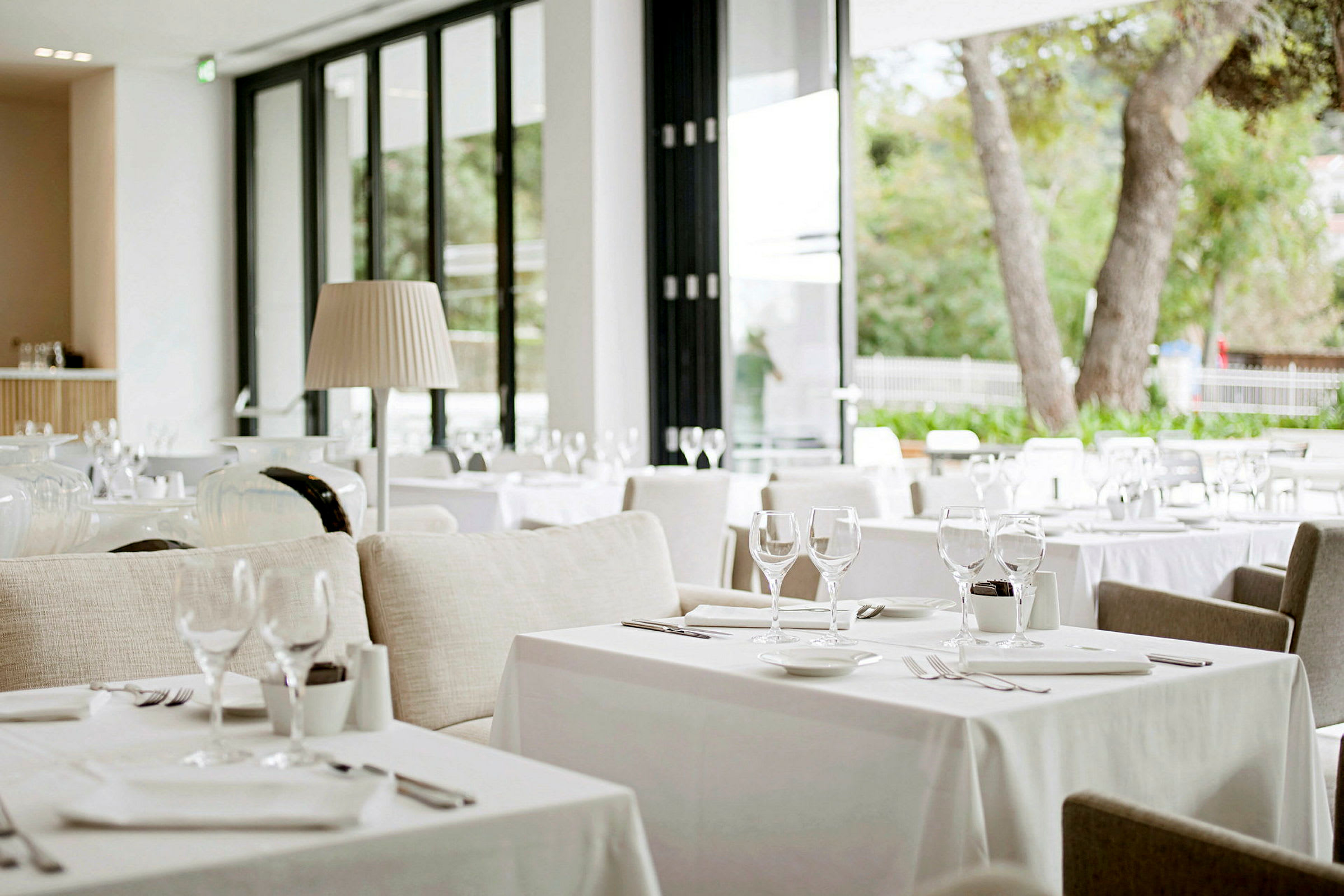 Bilde av en moderne og lys restaurant med dekkede bord og store glassvinduer som slipper inn naturlig lys. (AI-generert tekst)