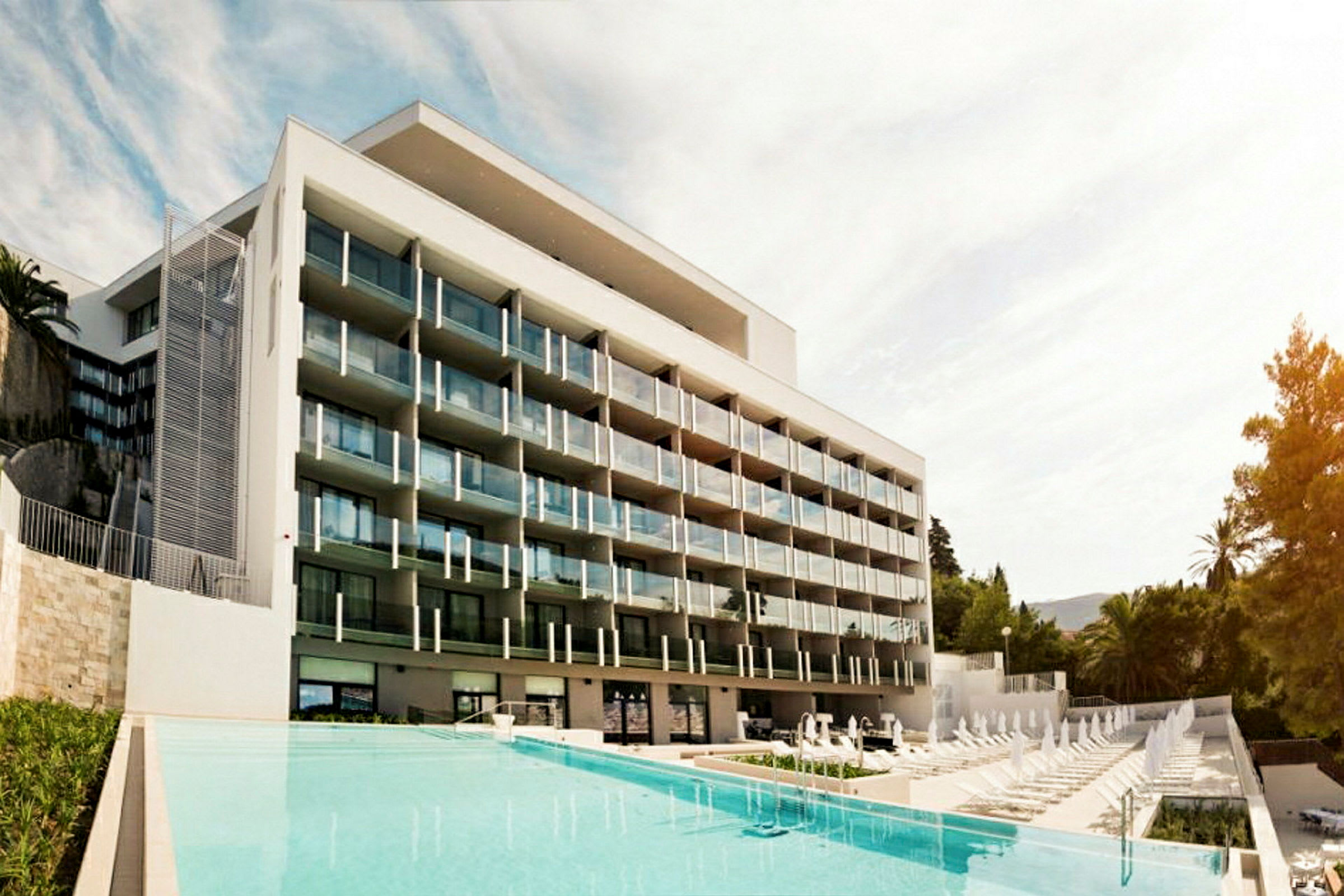 Et moderne hotell med flere balkonger foran et basseng. (AI-generert tekst)