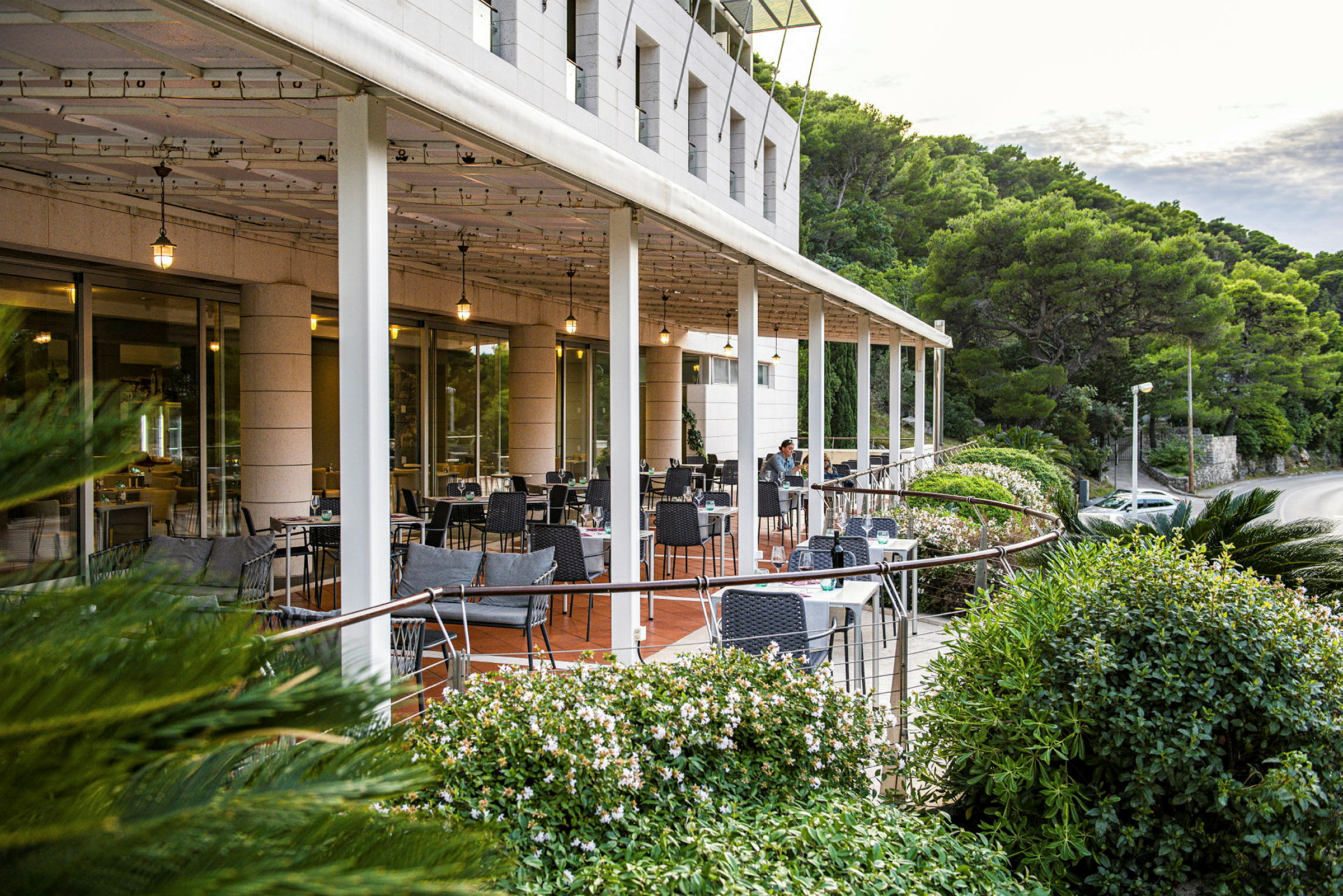 Restaurantterrasse med bord og stoler omgitt av grøntområder. (AI-generert tekst)