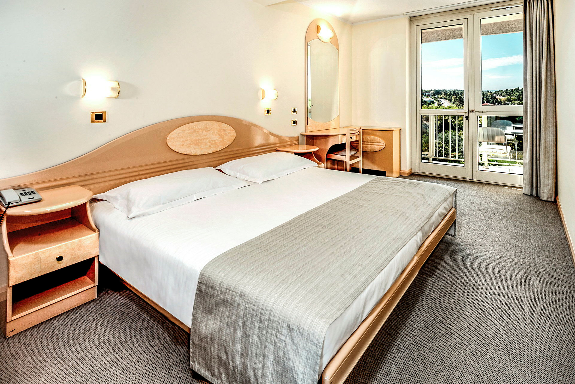 Et hotellrom med en dobbeltseng, et nattbord, et skrivebord og en balkong med utsikt. (AI-generert tekst)