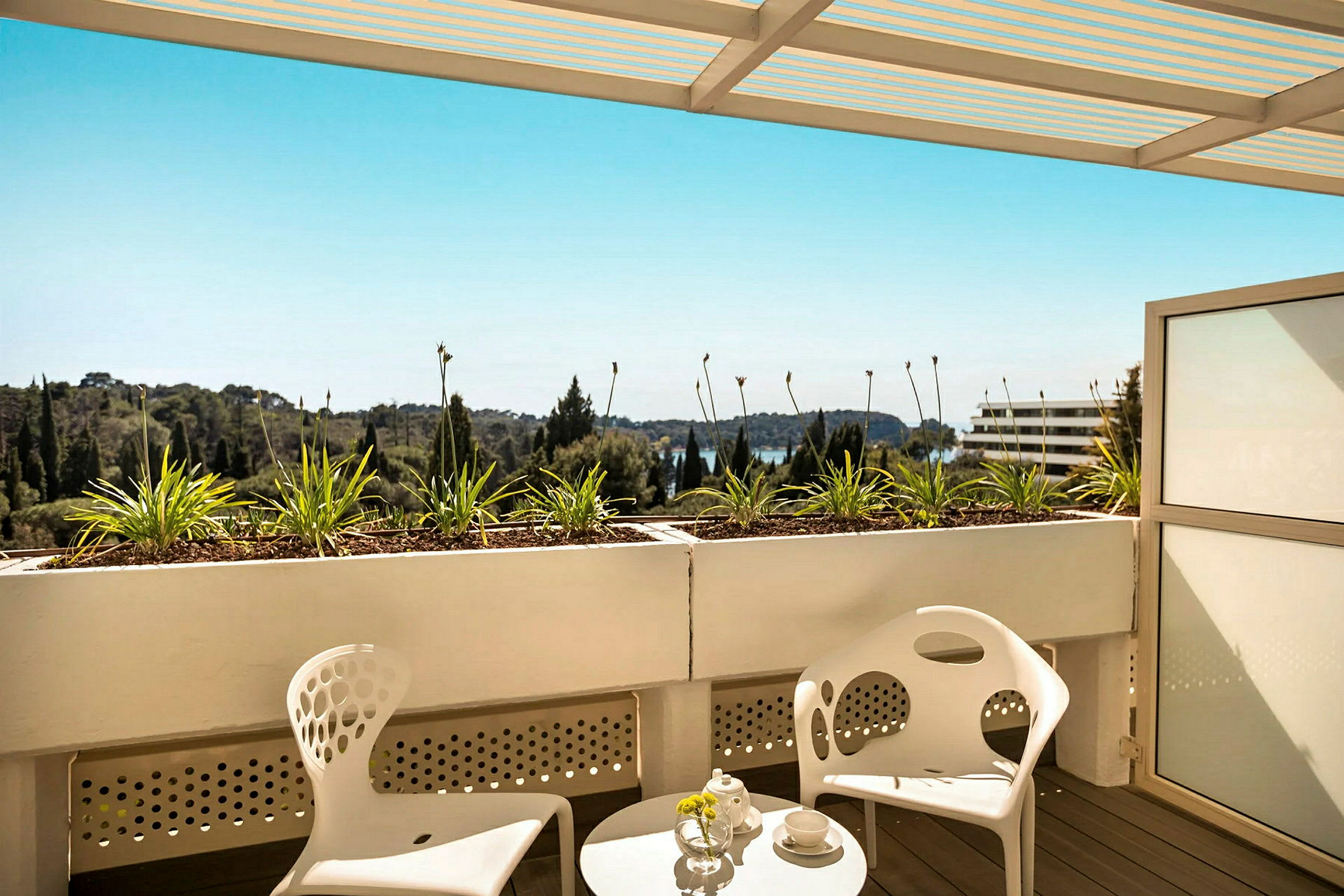 Terrasse med to moderne hvite stoler og et rundt bord, utsikt over grøntområder og blå himmel. (AI-generert tekst)