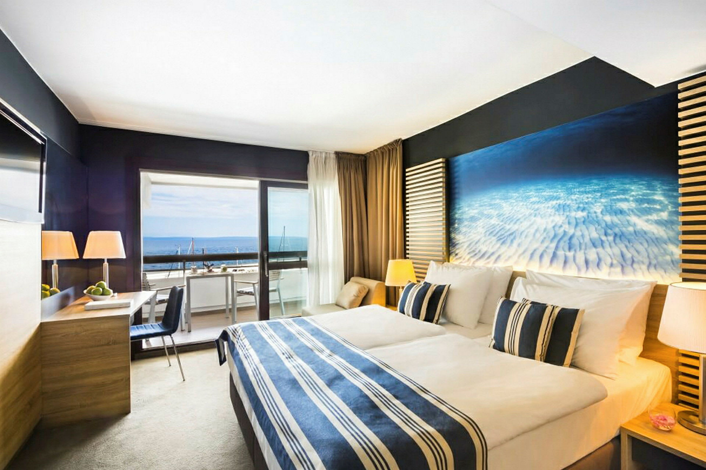 Et hotellrom med en dobbeltseng, moderne møbler og en balkong som vender ut mot havet. (AI-generert tekst)