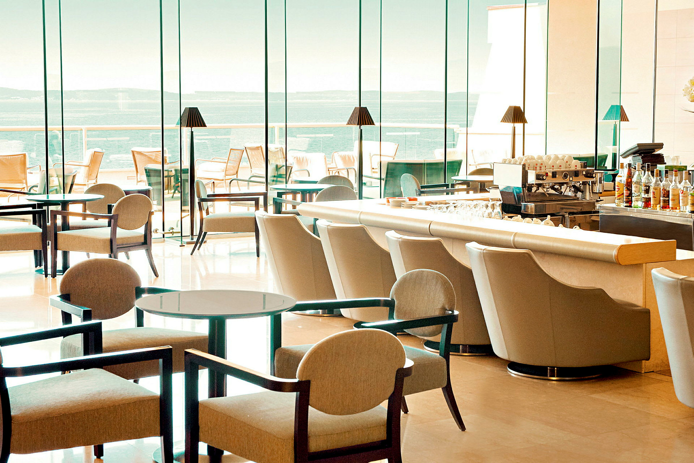 Hotellbar med moderne møbler og store glassvinduer med utsikt over havet. (AI-generert tekst)