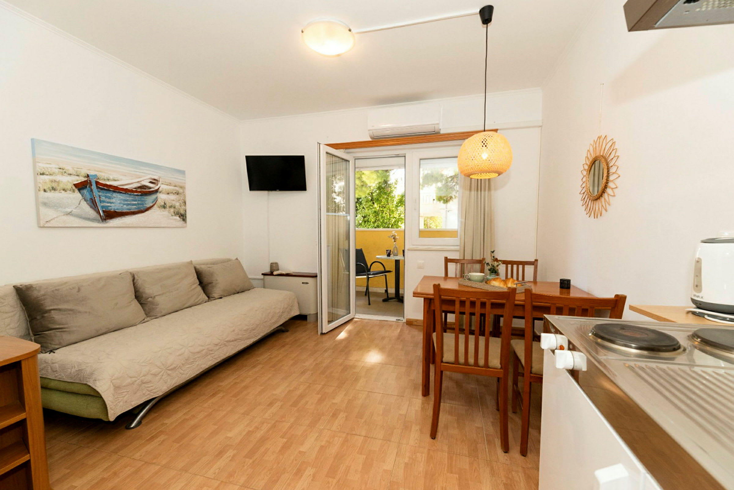 Et rom med en sofa, spisebord med stoler og dører som leder til en balkong. Et maleri av en båt henger på veggen. (AI-generert tekst)