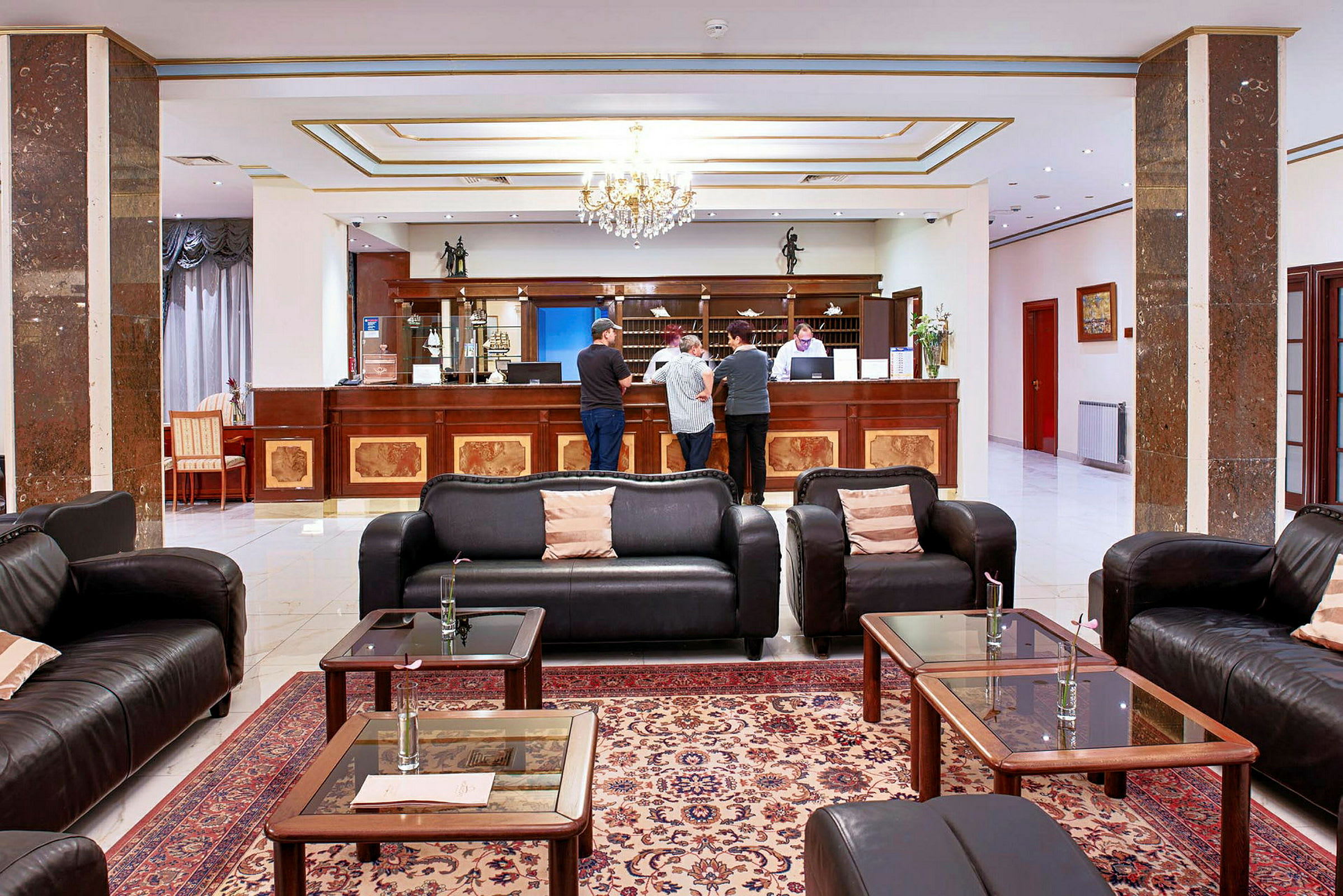 Hotellobby med sofaer, sofabord og resepsjonsdisk der flere personer står. (AI-generert tekst)