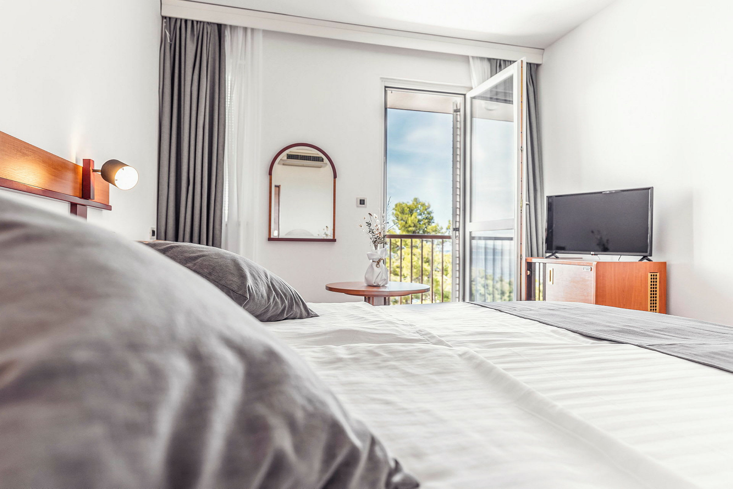 Hotellrom med seng, TV og åpen balkongdør. (AI-generert tekst)