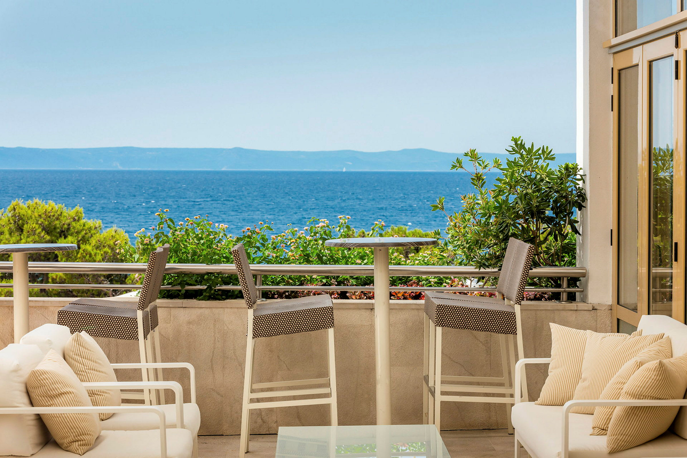Utsikt fra en terrasse med sittemøbler mot havet. (AI-generert tekst)