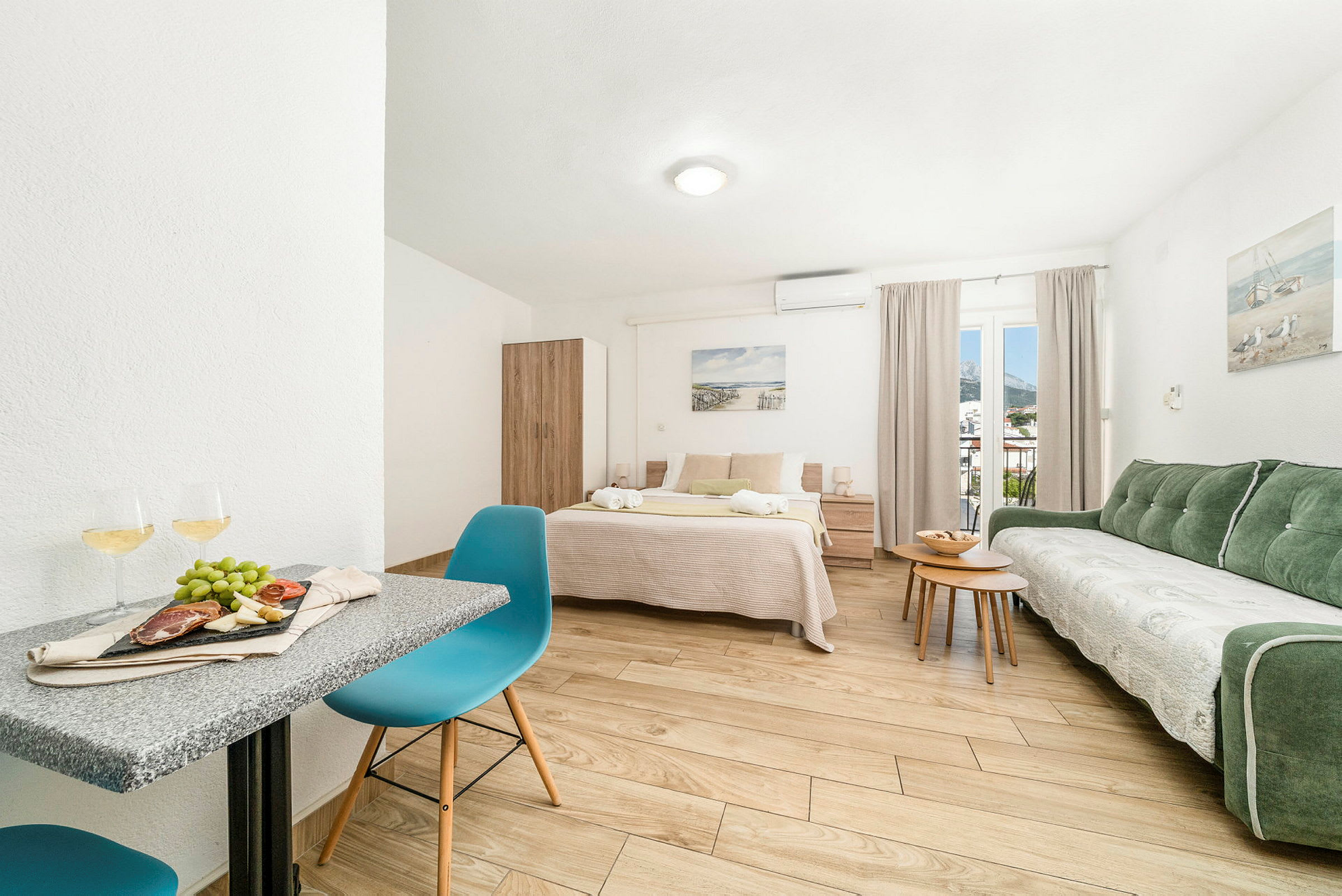 Et lyst og romslig rom med en dobbeltseng, grønn sofa, bord og stoler. Et nattbord står ved siden av sengen. Det er et vindu med gardiner. (AI-generert tekst)