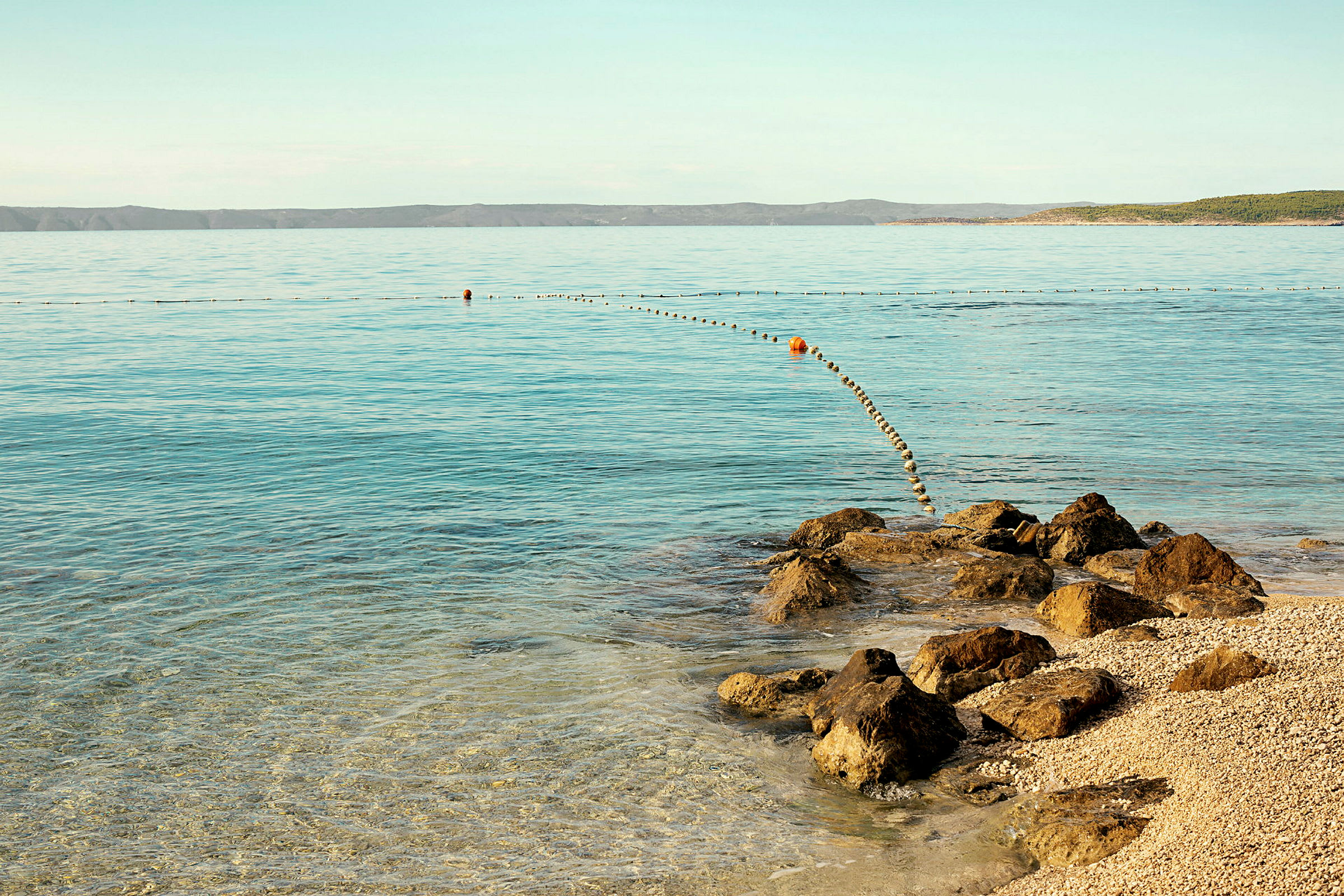 En steinete strand med rolig, klart vann som strekker seg mot horisonten. (AI-generert tekst)