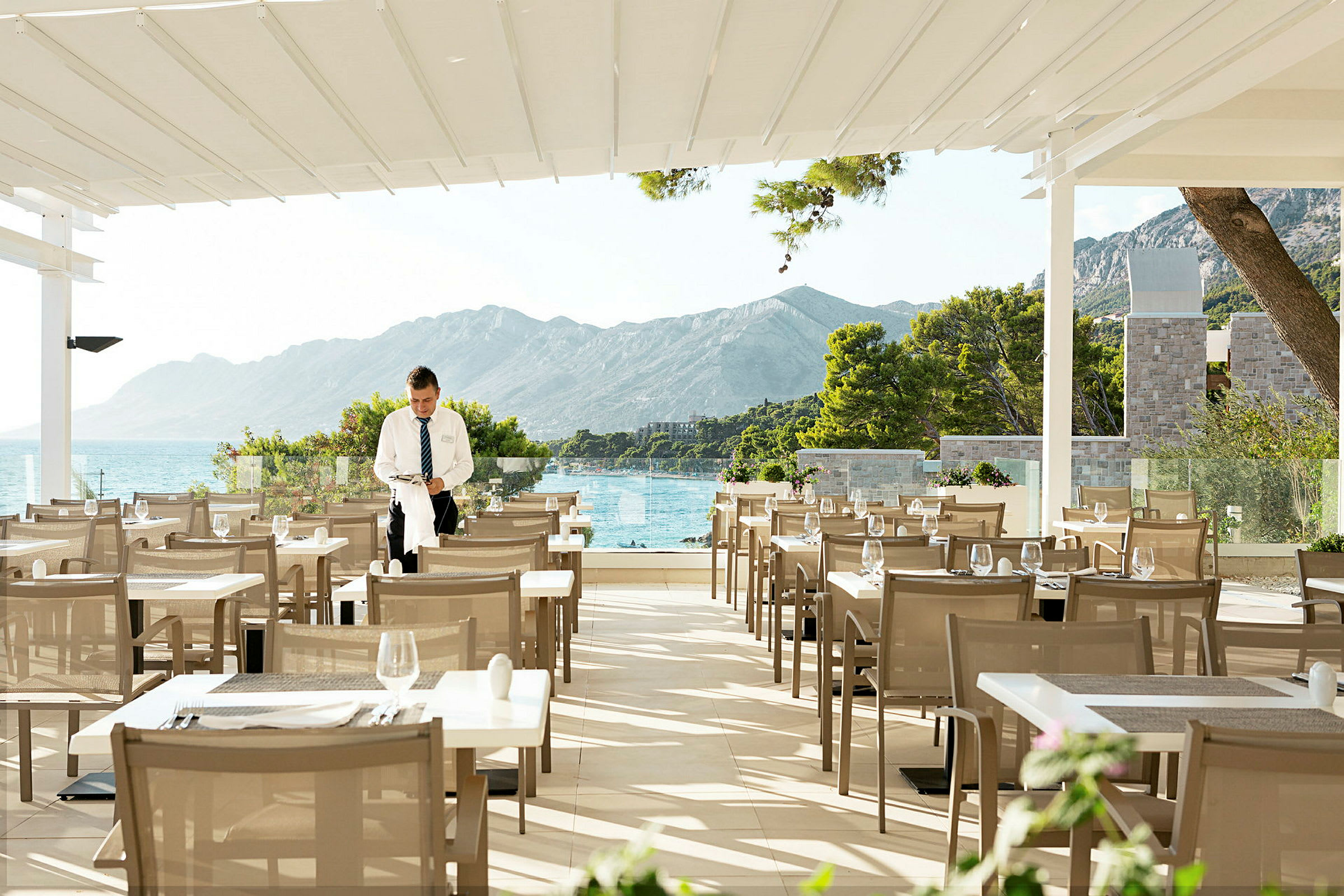 Restaurantterrasse med utsikt over havet og fjellene. (AI-generert tekst)