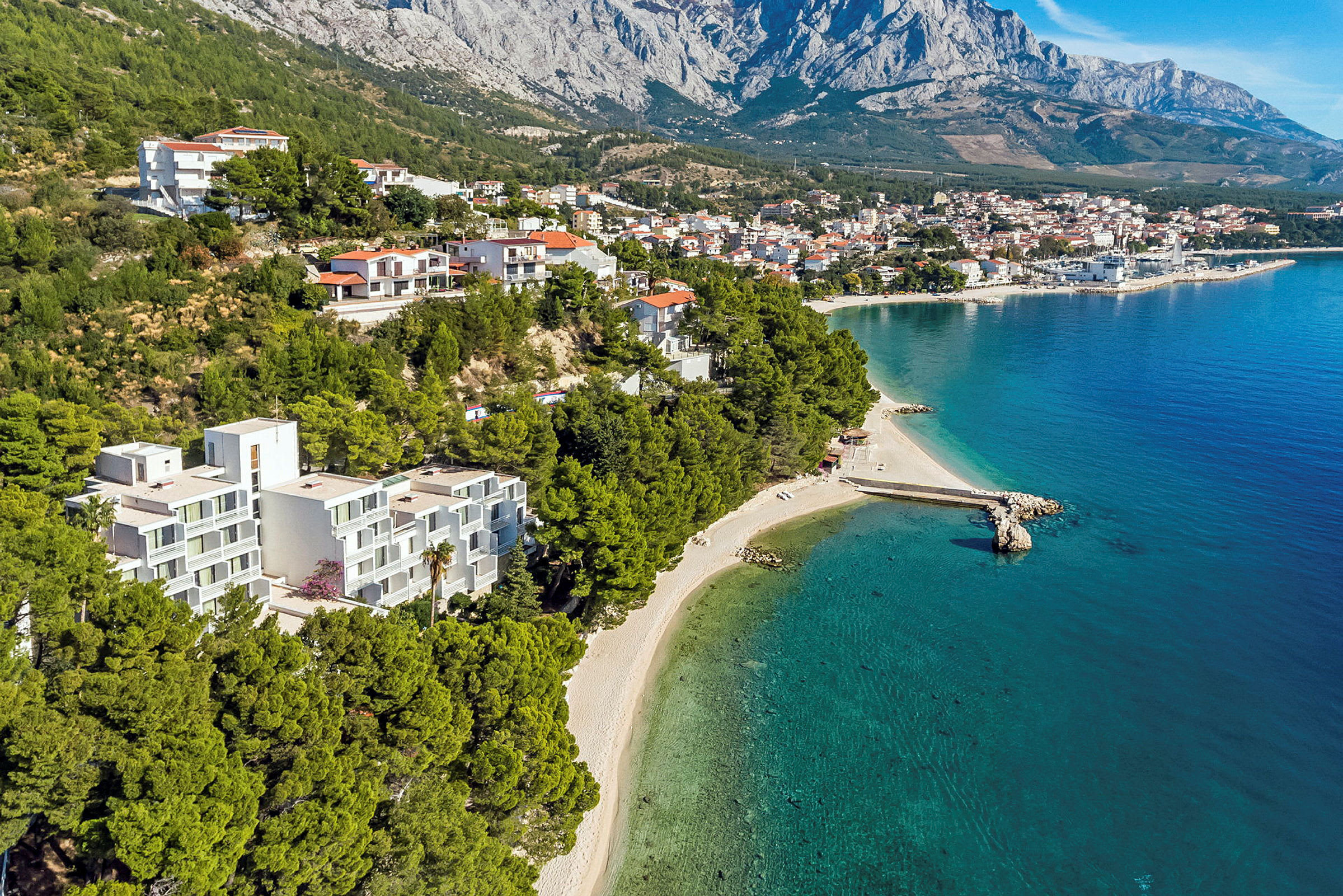 Utsikt ovenfra av en kystlinje med bygninger, strand og turkis hav med klare bølger. (AI-generert tekst)