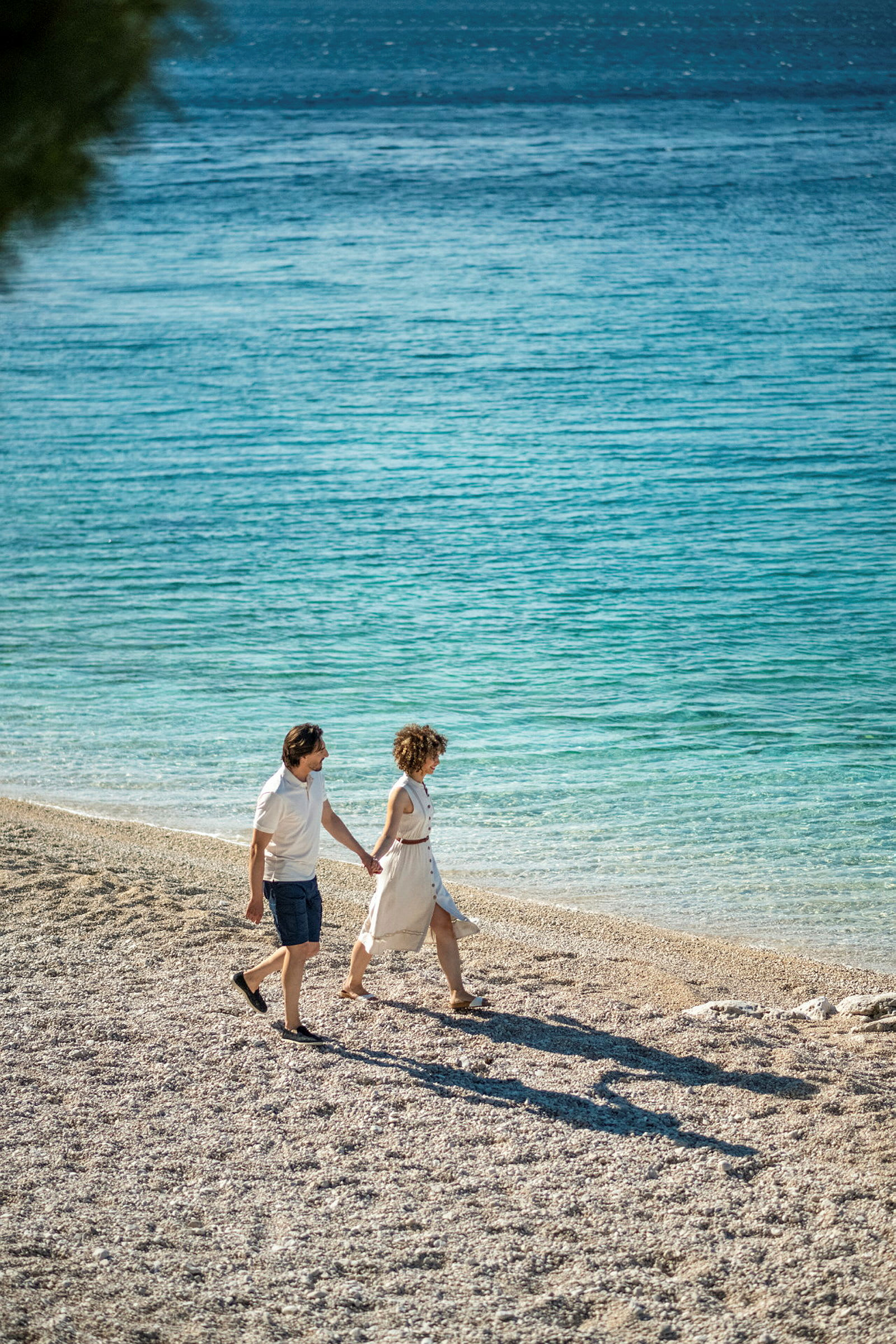 To personer går på en steinstrand ved sjøen. (AI-generert tekst)