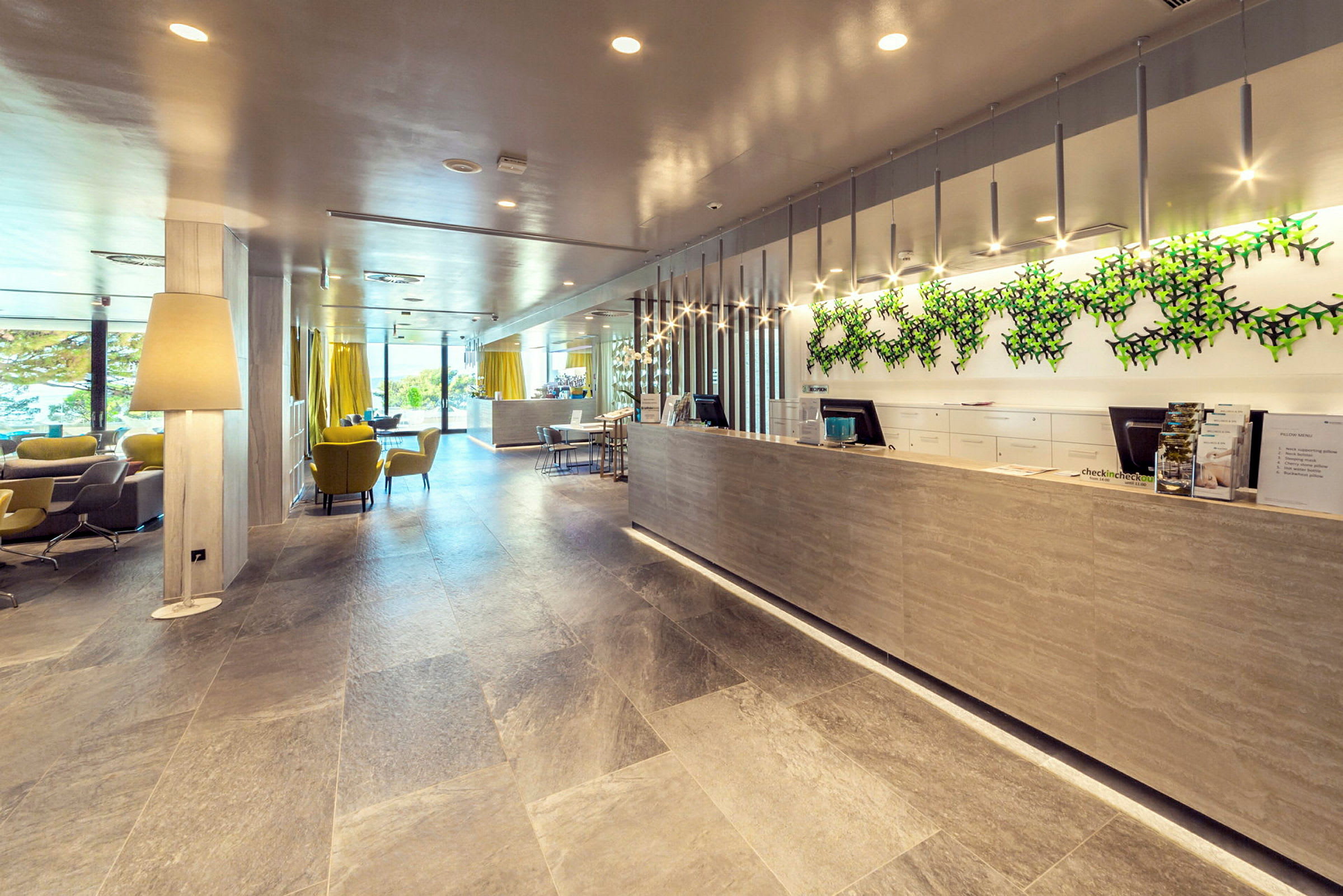 Resepsjonen på et moderne hotell, med sitteplasser, store vinduer og en dekorert vegg. (AI-generert tekst)